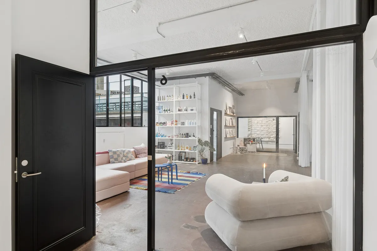 Kontor med åben og fleksibel planløsning, stor sofa, bord med lyse puder og lyse vinduer mod gården