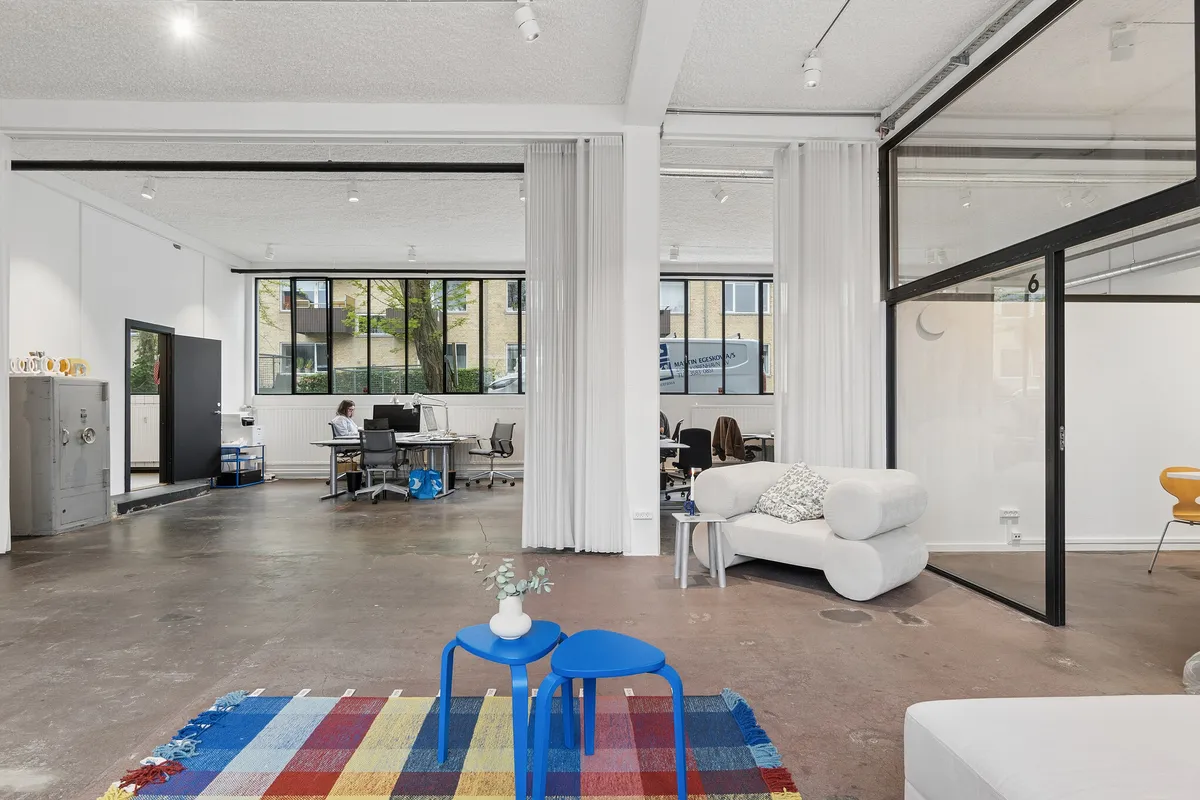 Kontorlokaler med åben planløsning og store vinduer. Stolene, skrivebord og sofaer med smuk tekstilbeklædning. Farverige gulvmåtter og moderne interiørdesign.
