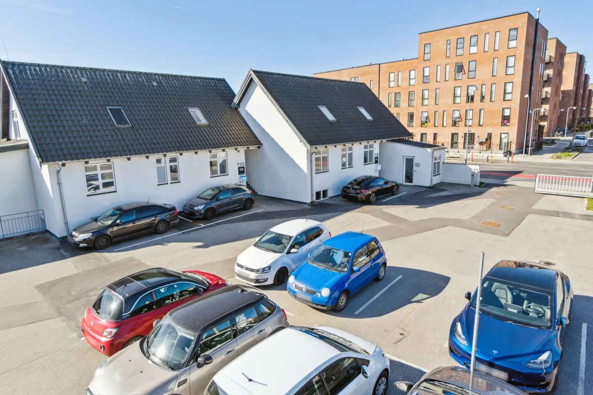 Lejemål med parkeringsplads til biler, hvor flere biler er parkeret foran huse med terrasser og skurtag