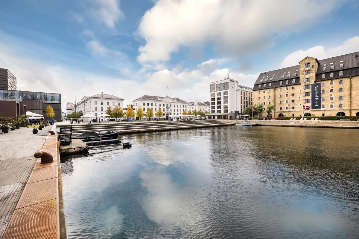 Moderne kontorbygning med røde tag og store vinduer i København, med lysthus og lysekroner, udsigt over kanal og vandflad og et lyst og solrigt vejr