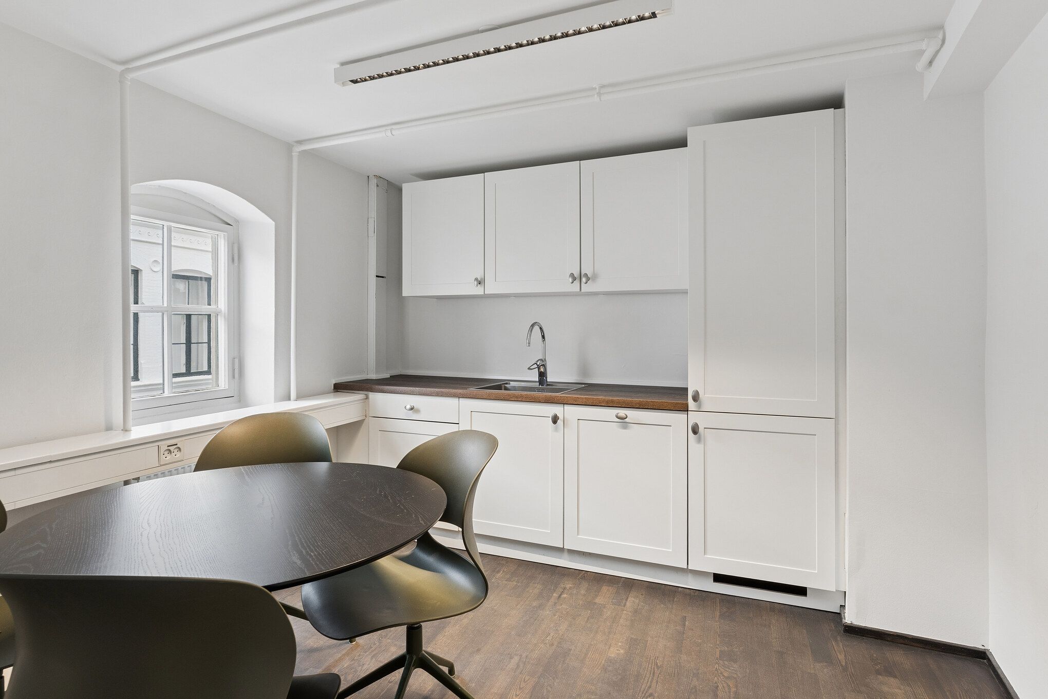 Nyrenoveret kontor med bord, stole og køkken med vandhaner i hvidt og brunligt design på 3. sal på Toldbodgade 12 i København
