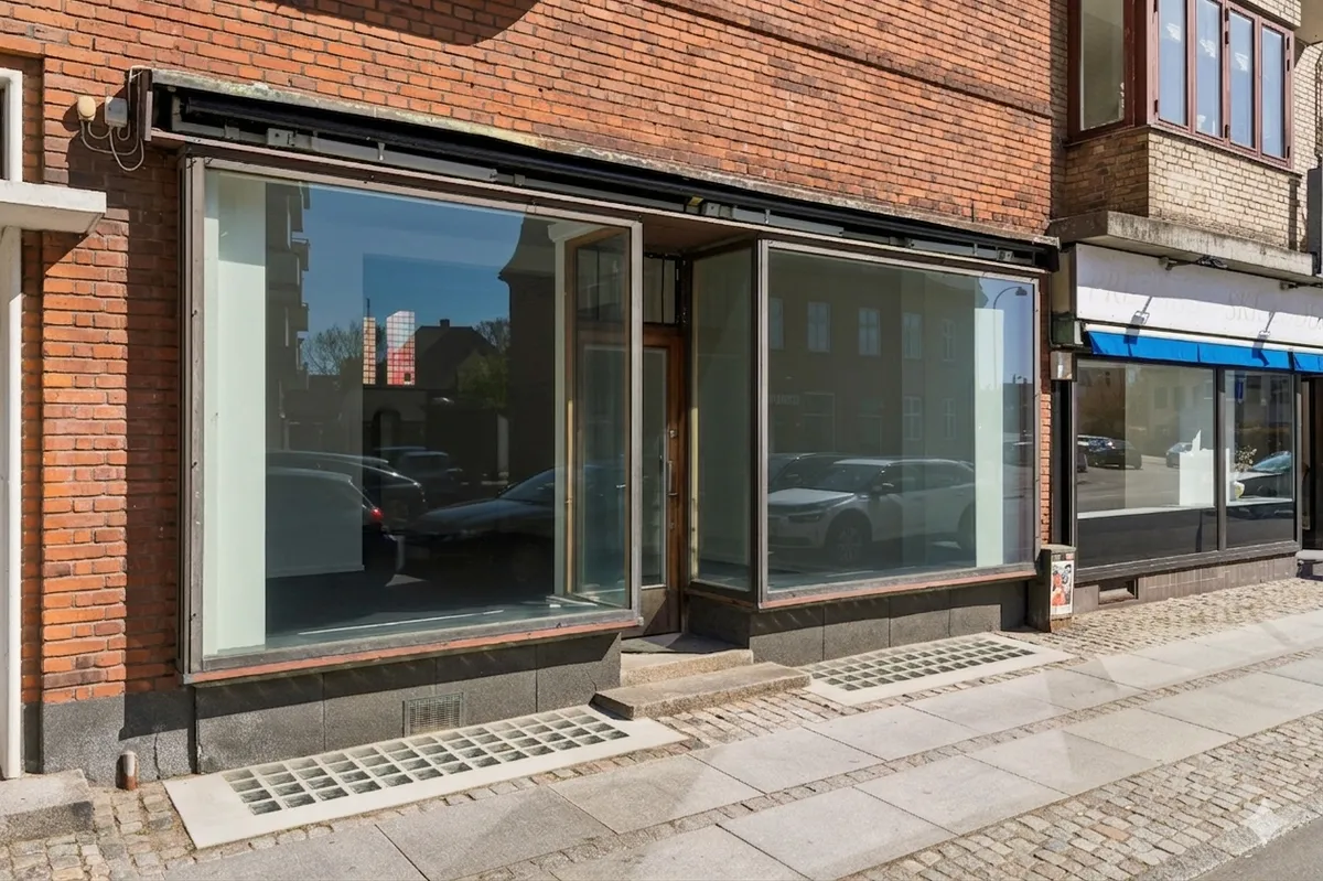 Foto af en butik med glasvinduer og en dør i røde mursten og gult cement. Et køretøj er parkeret foran butikken.
