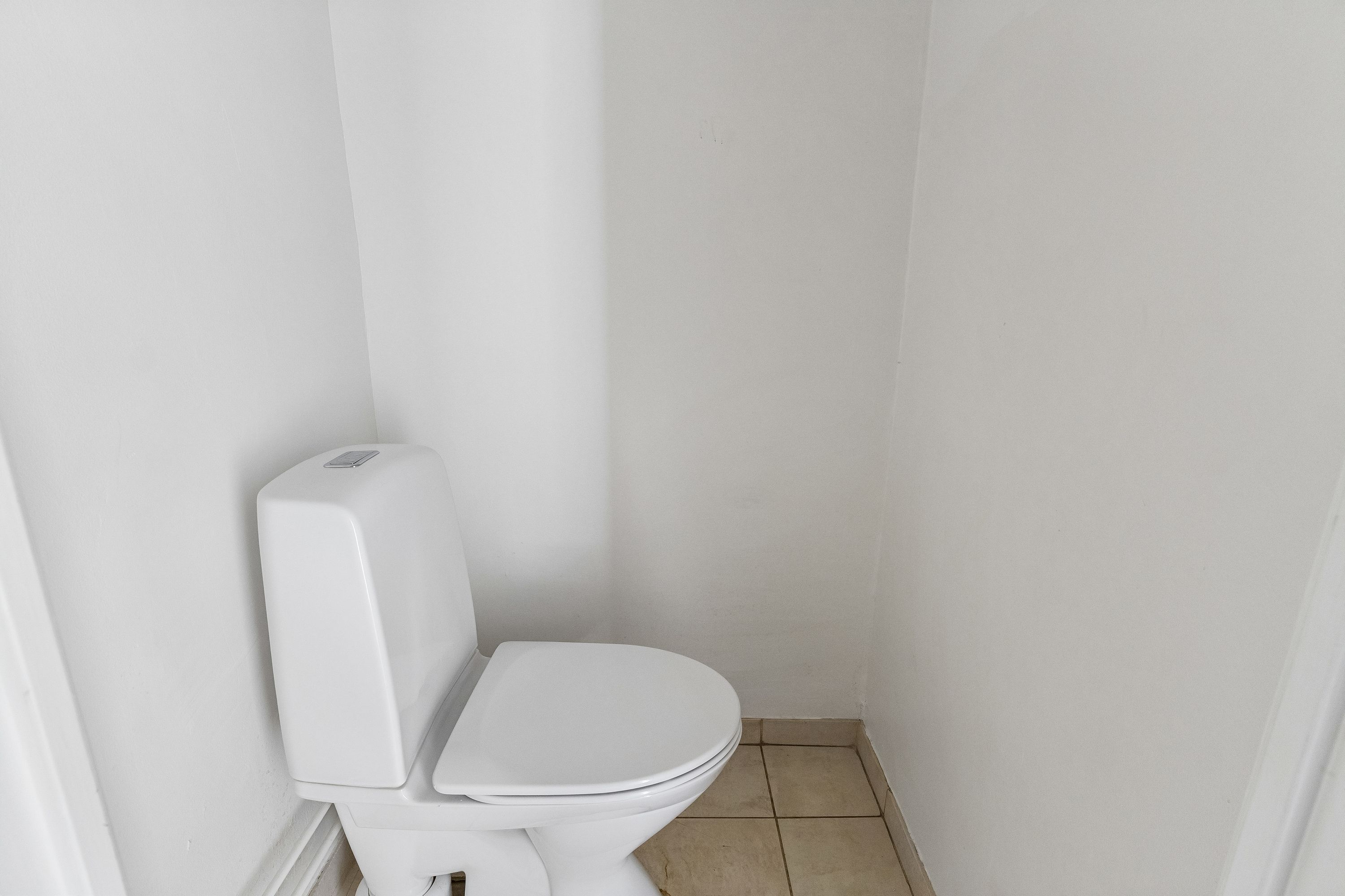 Et lille, rent og hvidt toilet med en hvid tank og en hvid toiletdæksel i en lille, hvidt malet toiletrum