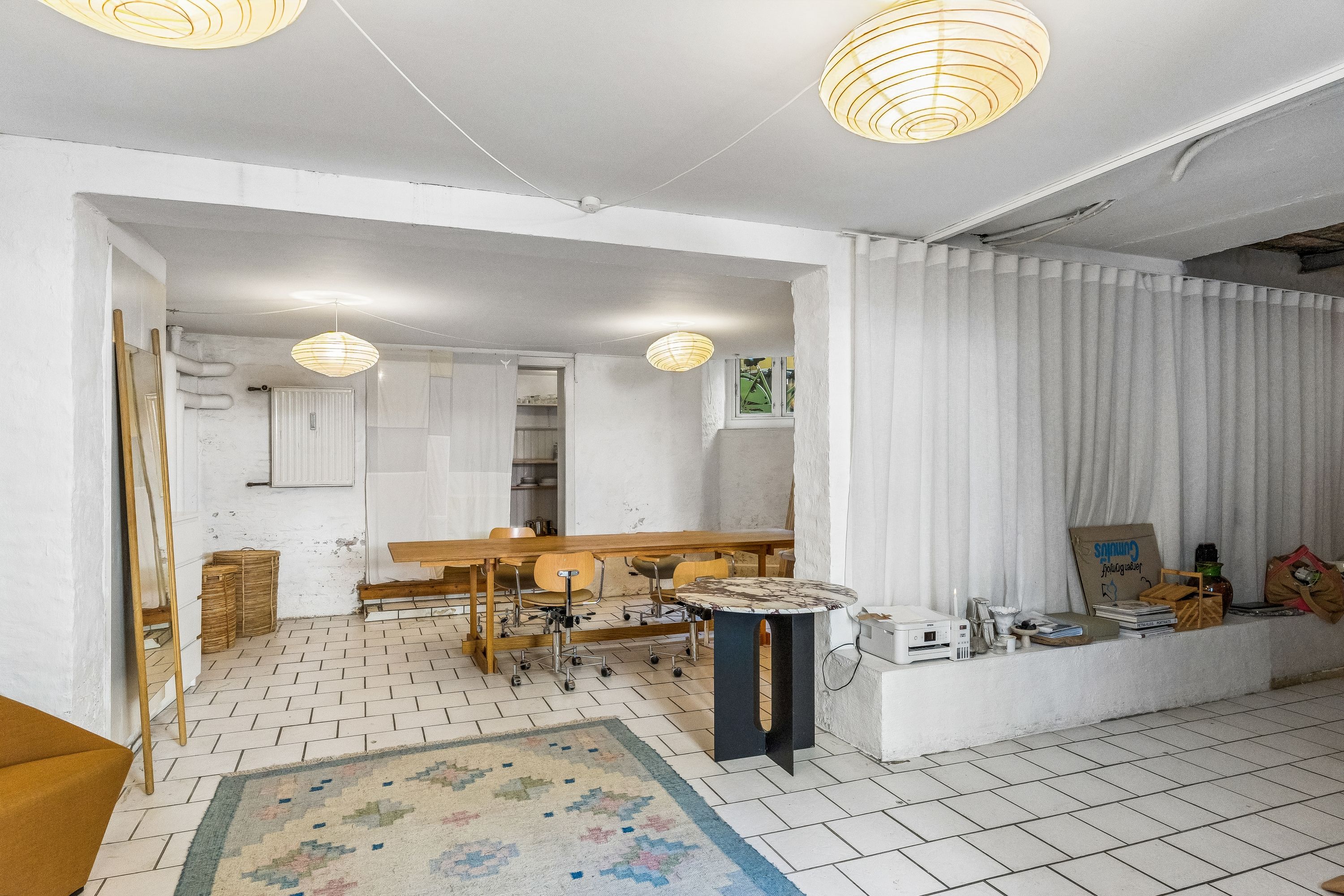 Ulejet lokale på Gothersgade med høj til loftet og moderne møbler. Et stort skrivebord og stole placeret i et hjørne. Dekorative lampekroner hænger fra loftet.