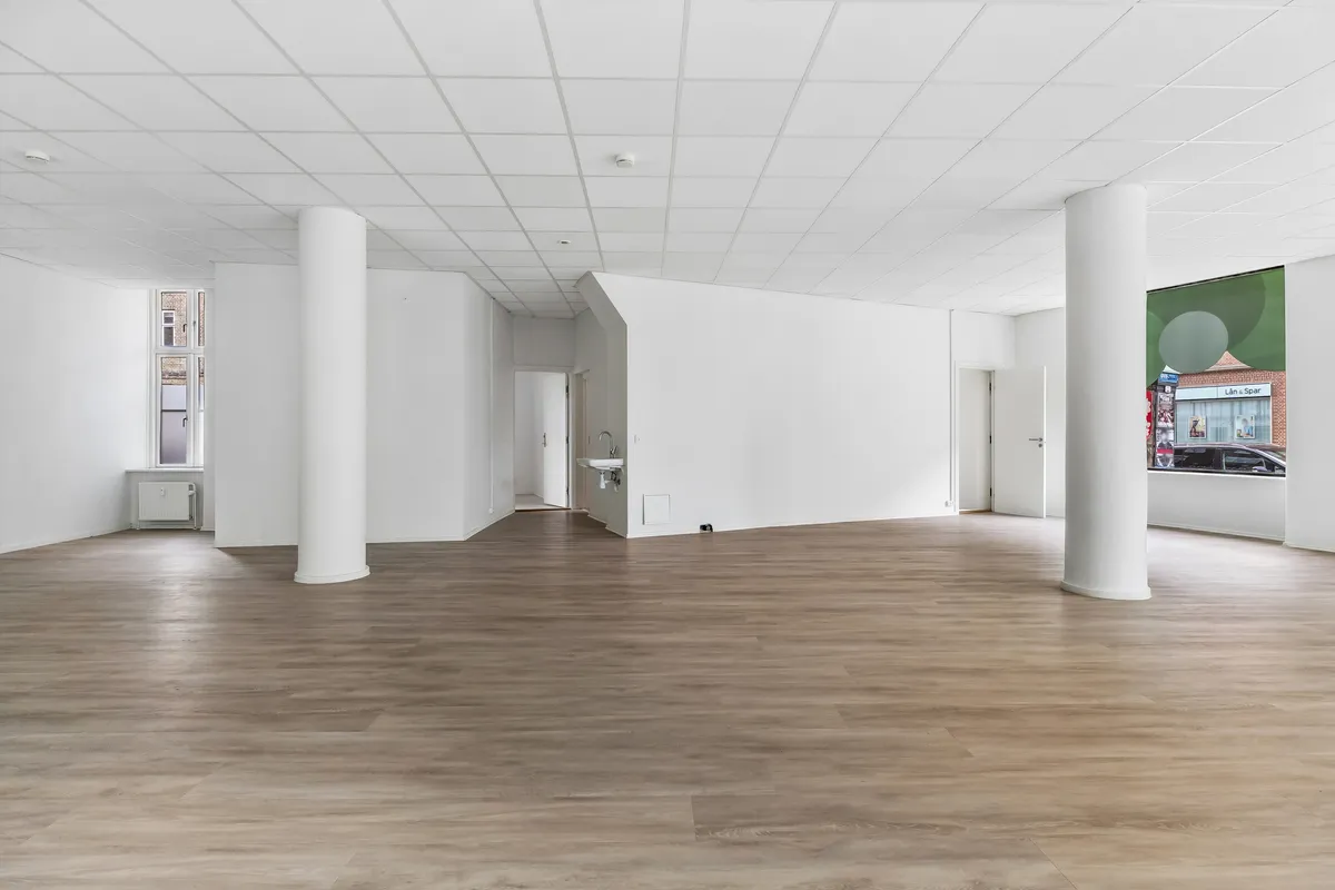 Store tomt med trægulve og høje lofter. Moderne, lyse interiør med hvide vægge og store vinduer. Hjørnevindu med udsigt til gade og biler. Simpel indretning med radiator og enkelt toilet.