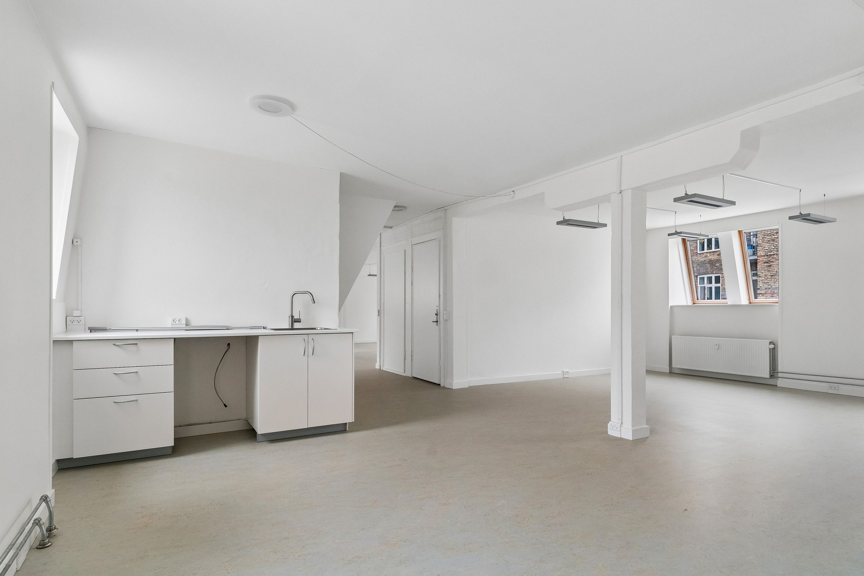 Lyst og funktionelt kontor med hvidt køkken, højloft, loftsvinduer, radiator og lyse indvendige vægge i Smallegade 46B, Frederiksberg