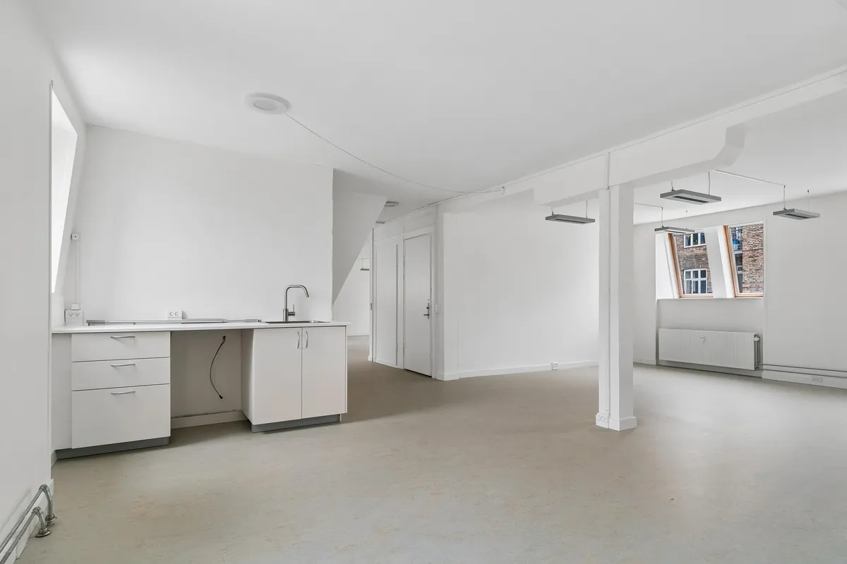 Lyst og funktionelt kontor med hvidt køkken, højloft, loftsvinduer, radiator og lyse indvendige vægge i Smallegade 46B, Frederiksberg