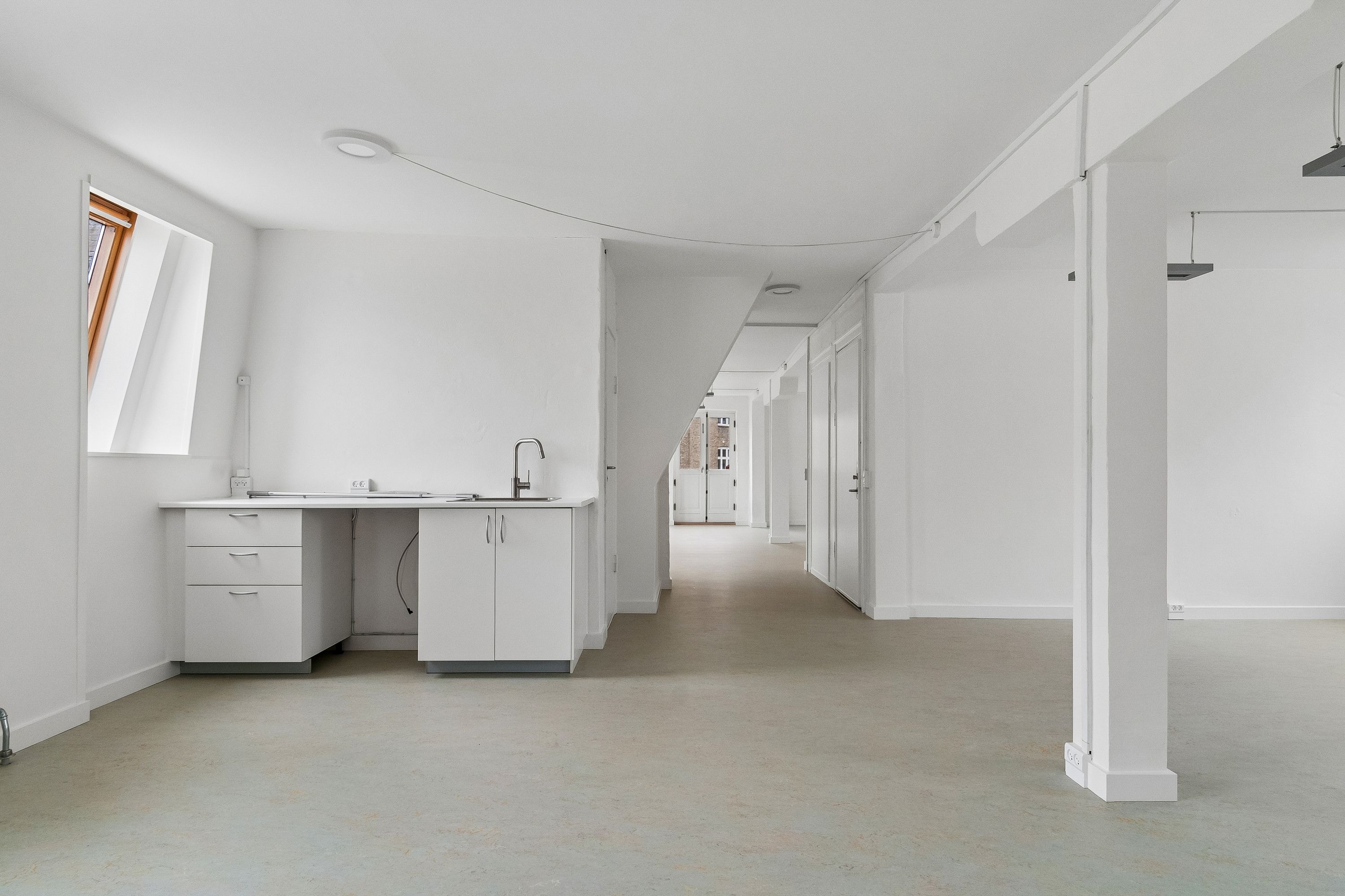 Lyst og rummeligt kontor med hvidt loft, hvide vægge, gulv og møbler samt lyse loftsvinduer og moderne, hvidt køkken