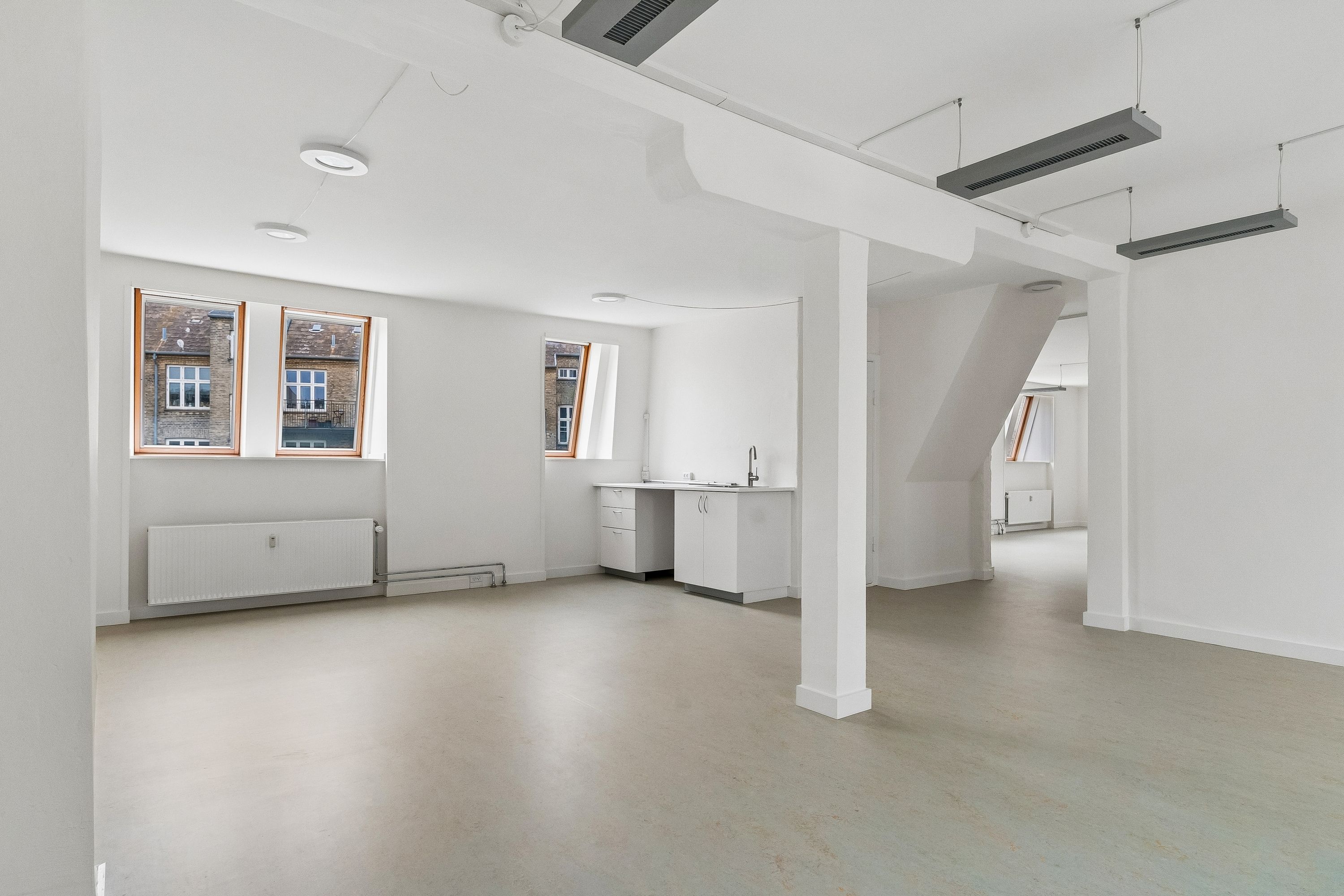 Lyst kontor med store vinduer og hvide vægge på Smallegade 46B. Rummelige lokaler med moderne møbler og nyttige faciliteter som radiatorer og køkken.