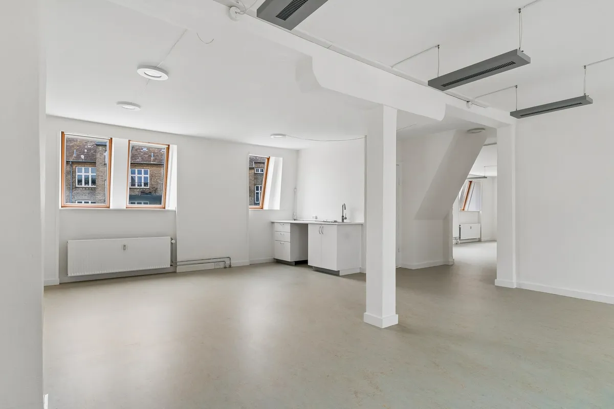 Lyst kontor med store vinduer og hvide vægge på Smallegade 46B. Rummelige lokaler med moderne møbler og nyttige faciliteter som radiatorer og køkken.