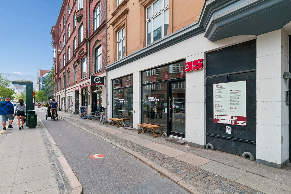 Folk går på fortov med restauranter, 35 Noodle Joint 35 med menu, cykel og mennesker, hjørne af gaden, slanke bygninger med vinduer og balkoner, lyse himmel