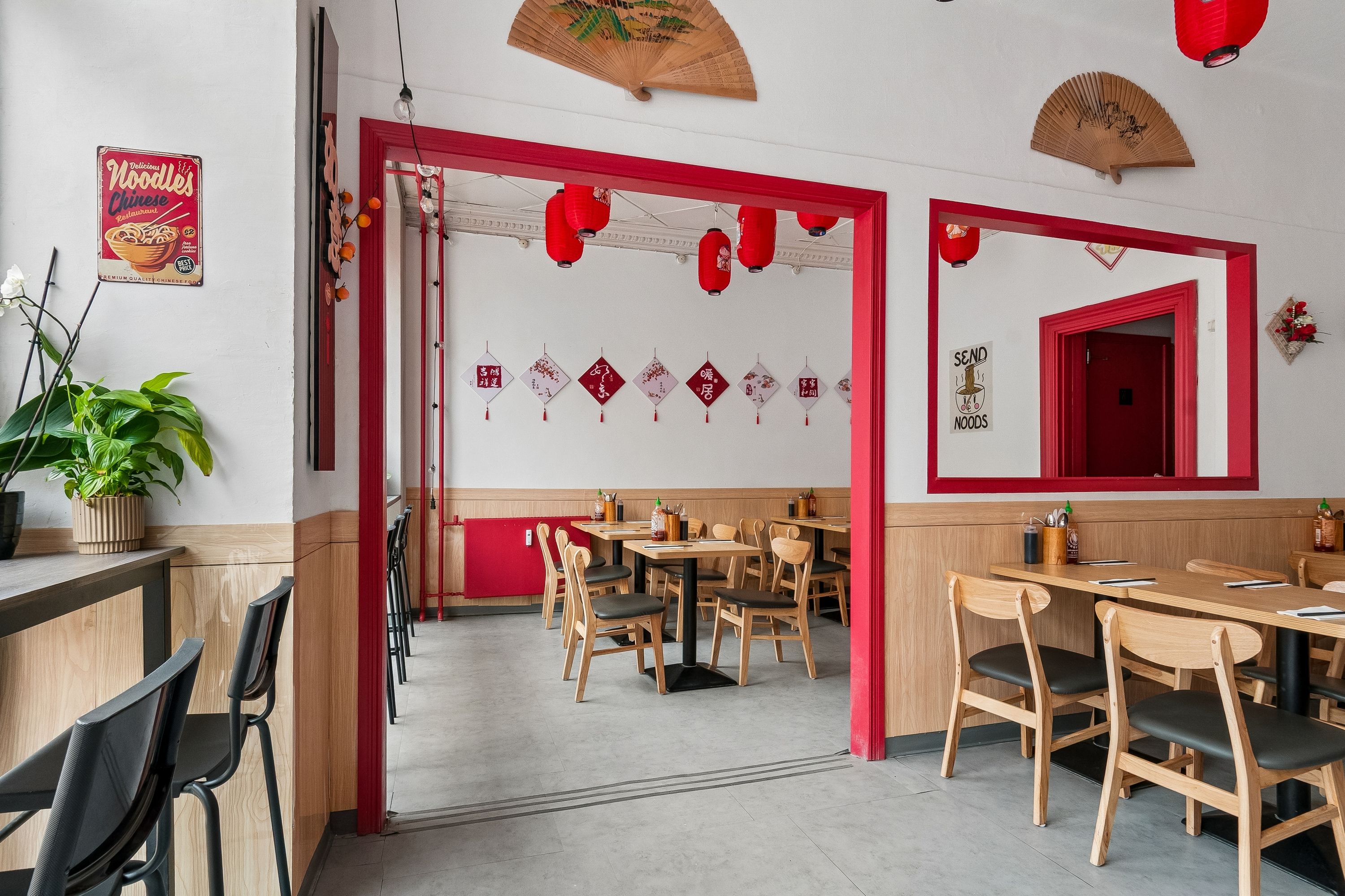 Moderne og pænt indrettet restaurant med røde døre, borde og stole samt vintage plakat og røde lanterner i loftet.
