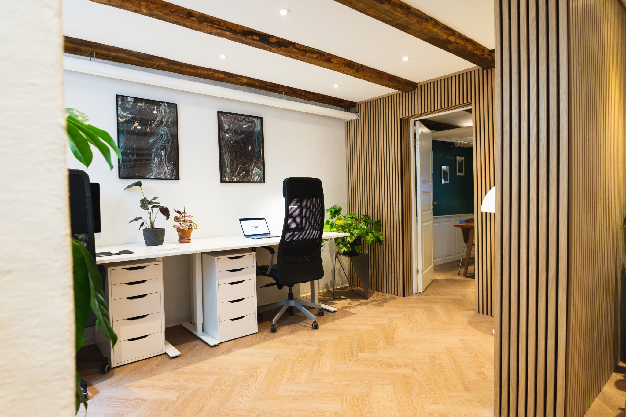 Kontor med højt til loftet, store vinduer og parketgulve. Kontorbord med 2 stole, 2 plantepot og 2 billeder på væggen