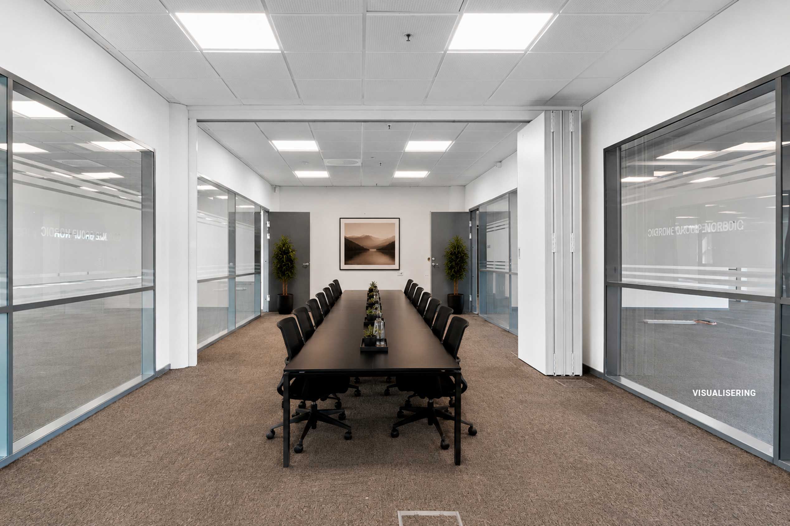 En stor møde- og konferencesal med bord, stole, gulvbelægning og to planter i hjørner samt et landskabsbillede på væggen