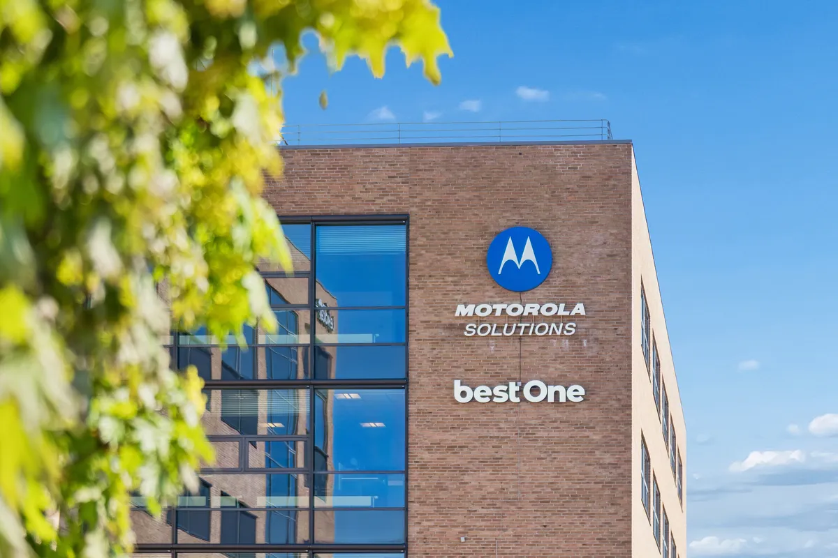 Motorola Solutions bestOne bygning med solsikkegul facade og blå logo. Lysindfald og glasvinduer reflekterer i glas. Lysblå himmel med få skyer
