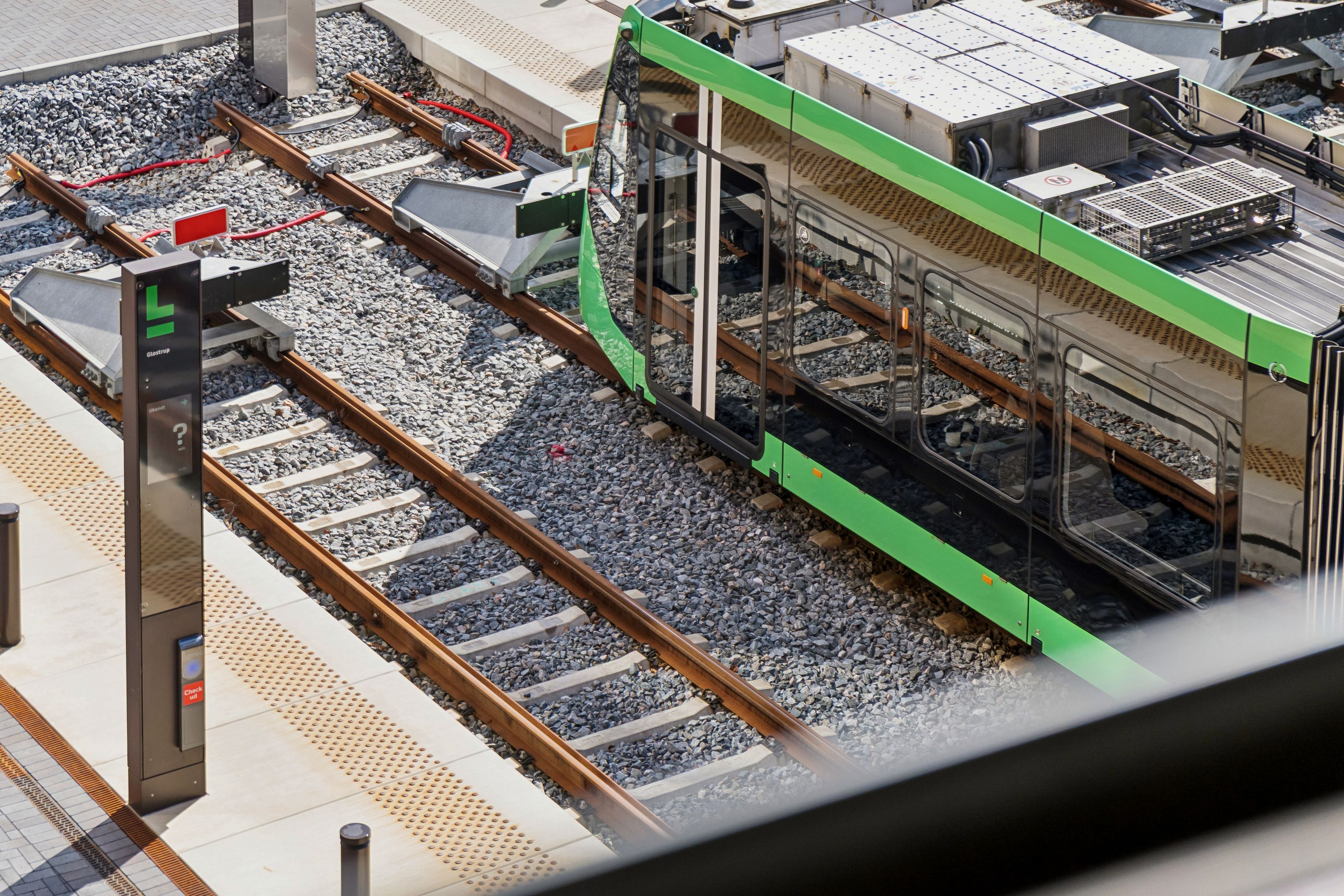 Et moderne kontorrum med lyse, åbne ruder og lysindfald i Glostrup. Et spor med letbanen og nye, moderne kontorer. En infoskilt med en spørgsmålstegn står på perronen.