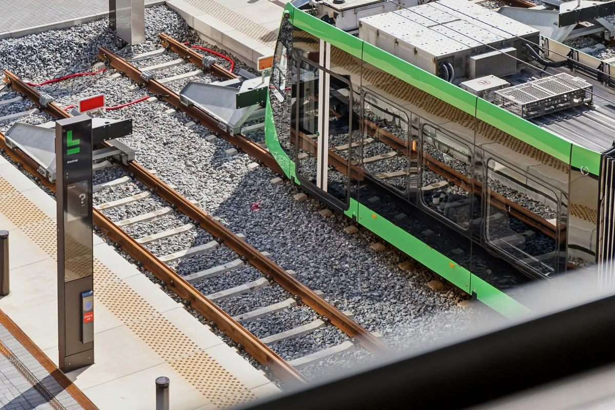 Lyserød og grøn sporvogn er i bevægelse og kører på jernbanesporene i Glostrup Station, hvor sporvognen reflekterer i sine vinduer.