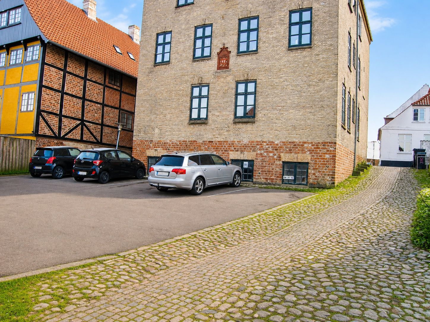 Investering til salg på Slotsgade 21 i Haderslev med tre parkerede biler og en stenbro foran huset med mange vinduer