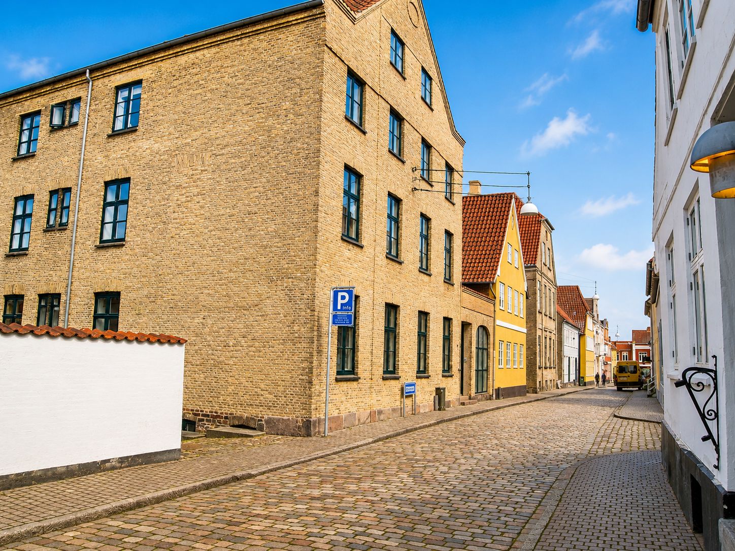 Investeringsejendom med røde tegltag, lysegul facade og parkeringsskilt på Slotsgade i Haderslev. Et gammelt gult buskørende bus er i fjernheden