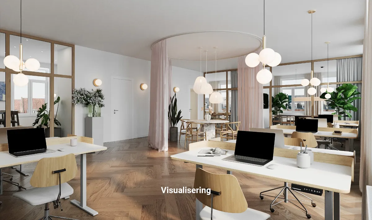 Kontorbord med computer, bøjle og lampe i en stilfuld kontor med parketgulv og lyse lysekroner. Væggen er hvid og der er plante i potte.