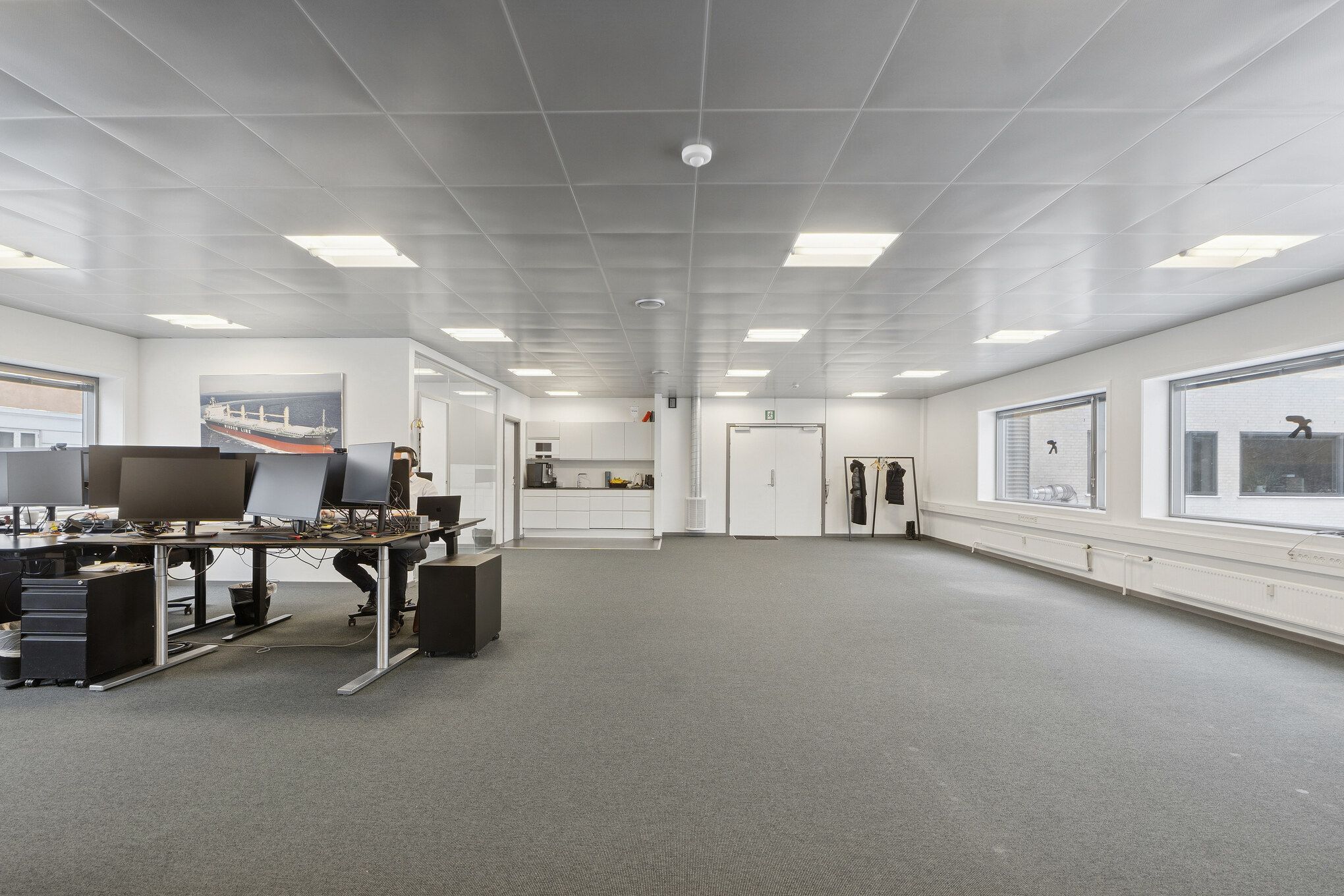 Åbent kontor med moderne udstyr og teknologi på højde med de seneste trender. Billeder og tekst på væggen forbedrer arbejdsmiljøet. Gode lysforhold og lyse gulve.