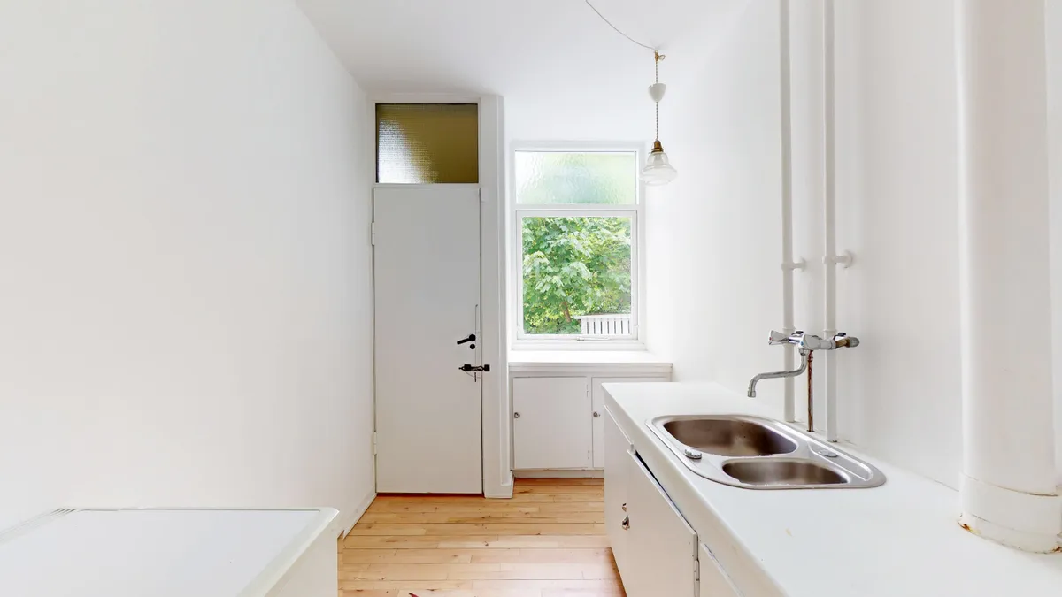 Moderne renset køkken med hvidt design, lyse vinduer og lysekroner i loftet. Trægulv og en dobbeltvask med rustfrit stål og lysekroner.