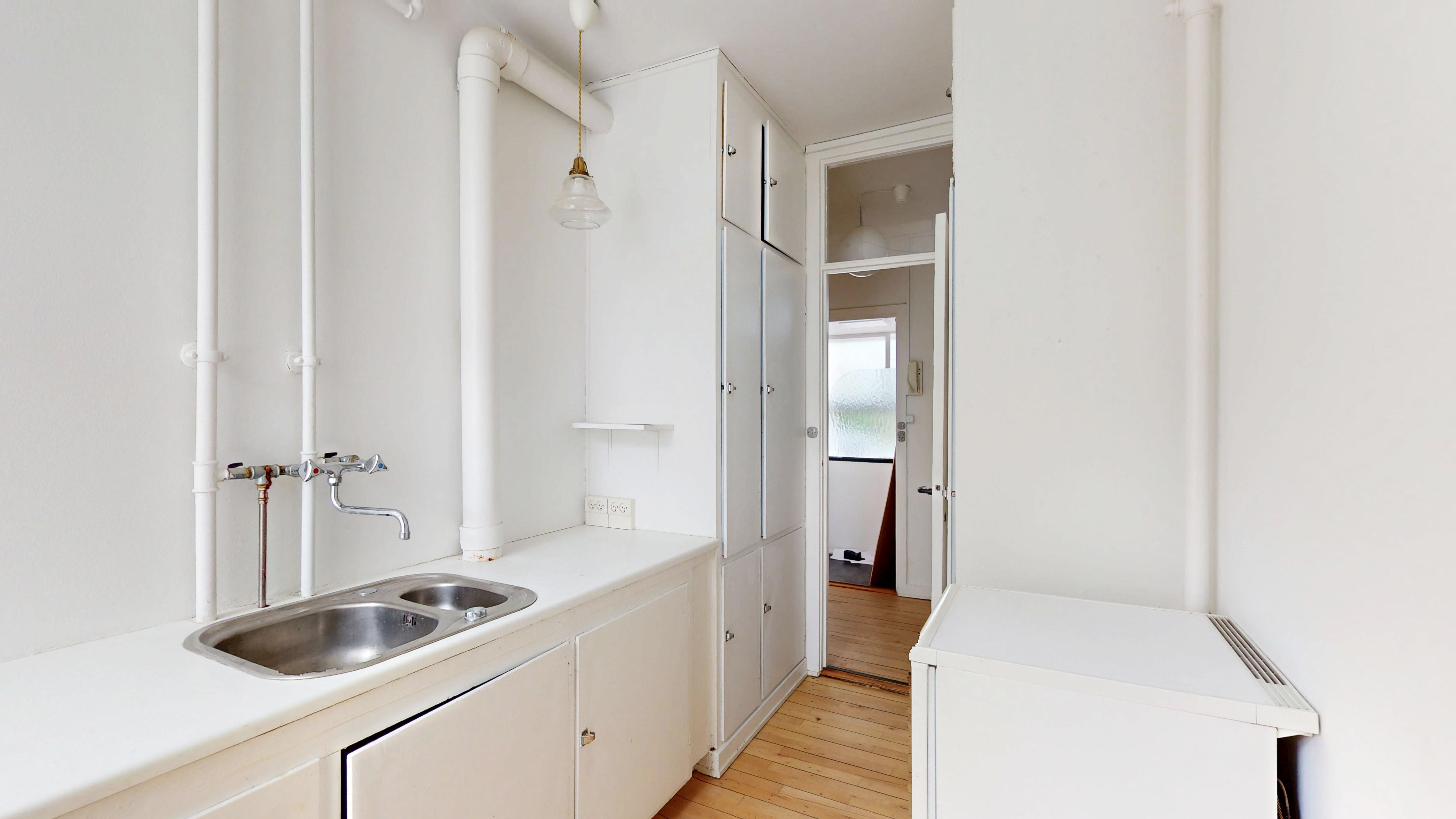 Hvidt kontorlokal med dobbeltvask og lysekroner i loftet. Køkken med sink og p-trap. Døre og vinduer giver masser af dagslys til rummet.