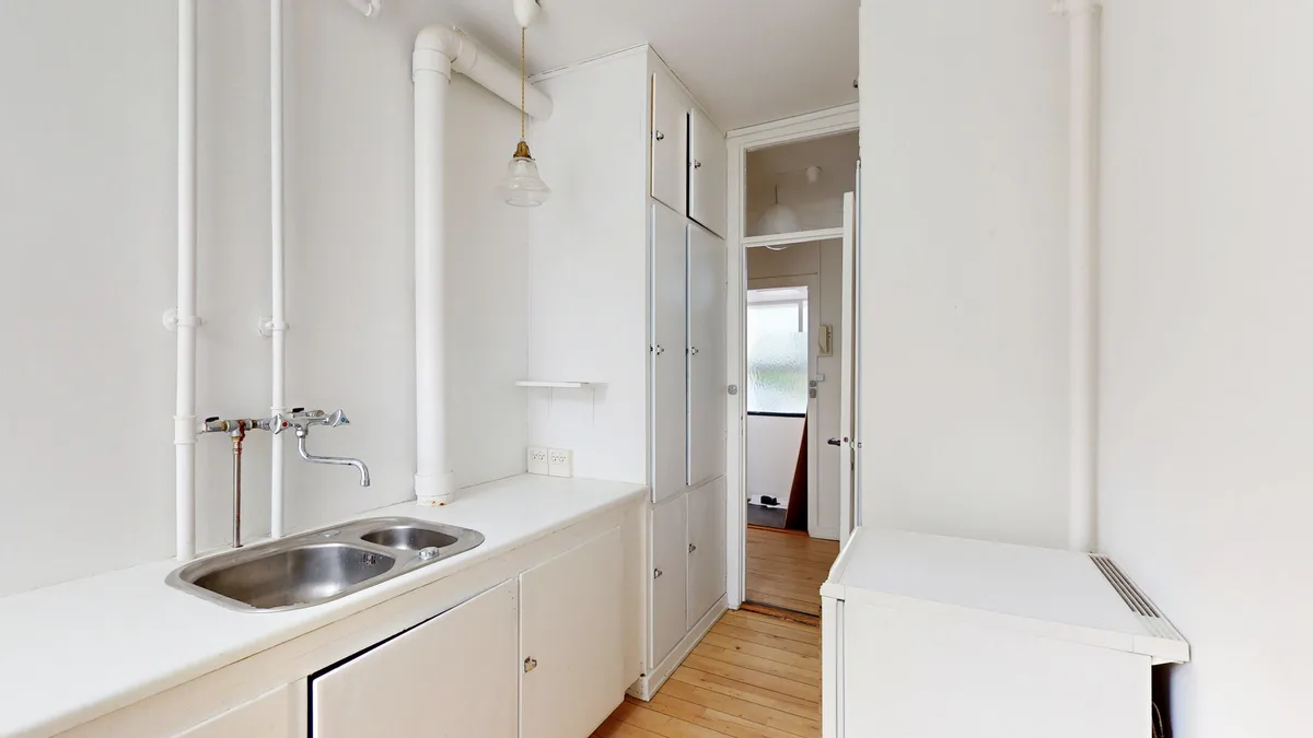 Hvidt kontorlokal med dobbeltvask og lysekroner i loftet. Køkken med sink og p-trap. Døre og vinduer giver masser af dagslys til rummet.