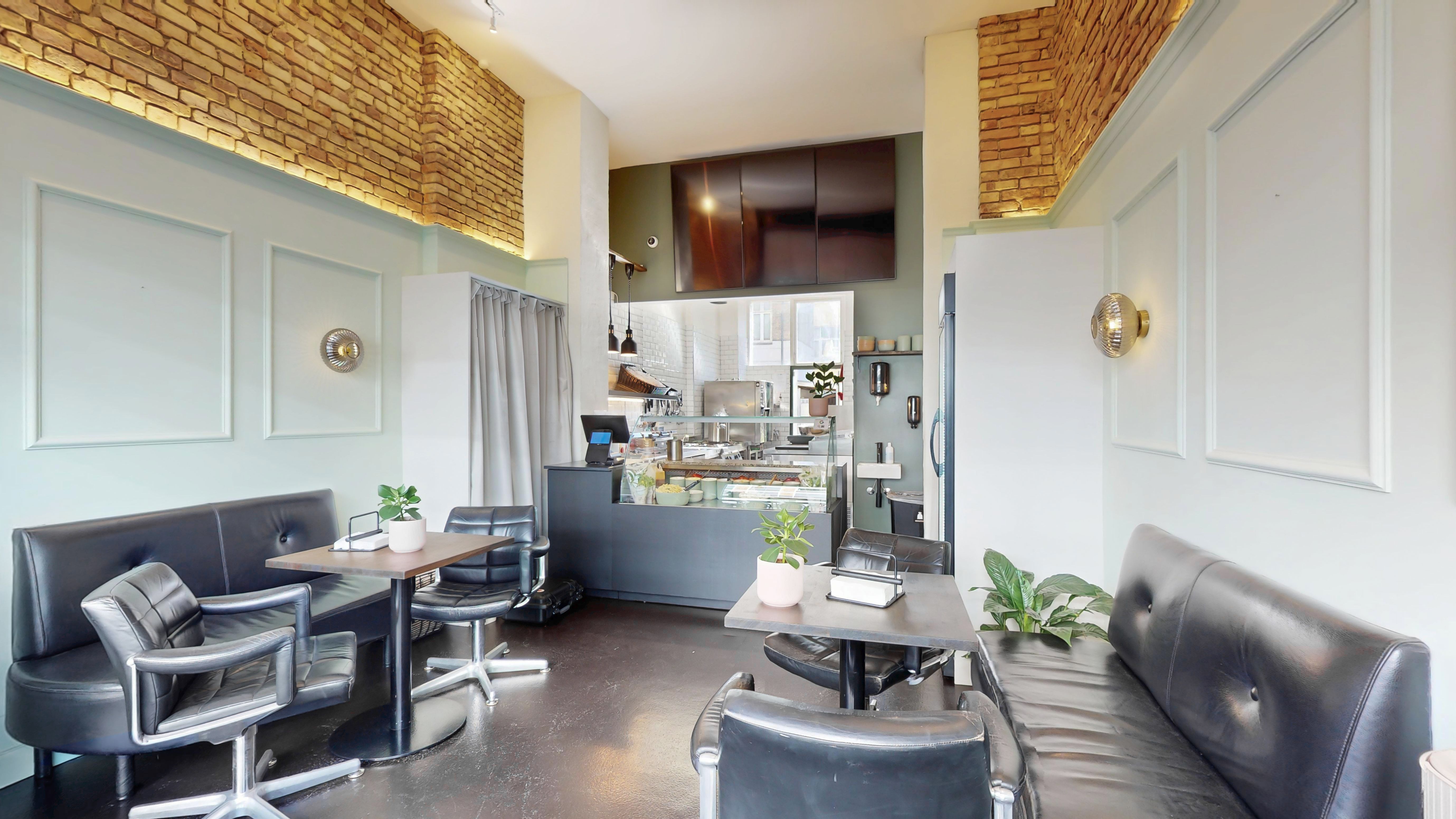 Moderne café med højt loft og lyse vægge. Bord og stol arrangement med plante og dekorative lys. Bag servitriceskranken står apparater og et køleskab.