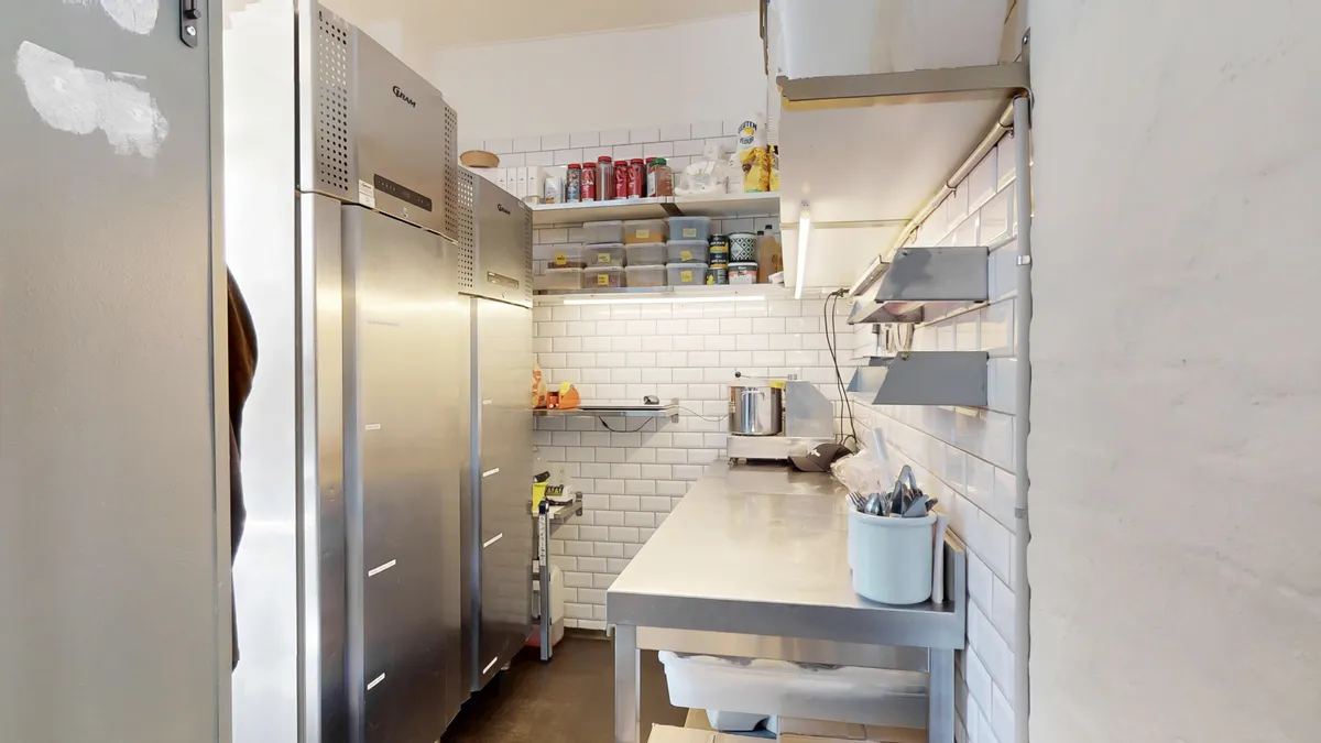 Et foto af et moderne café køkken med flere husholdningsapparater, køleskabe og et udstyret arbejde.