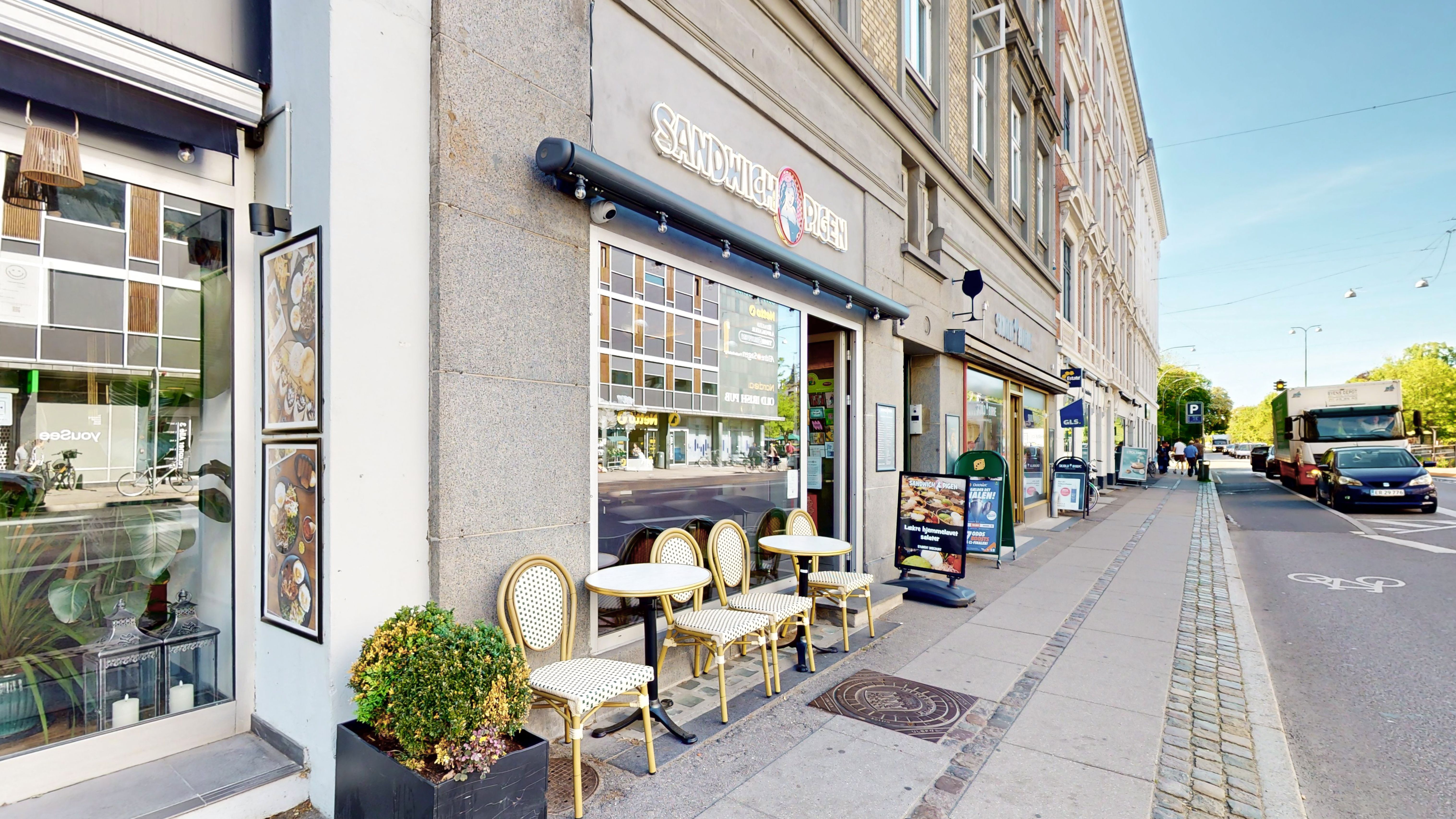 Cafe med terrasse med sædestole og spisesteder udenfor et restaurantvindu med reklameskilt og menukort