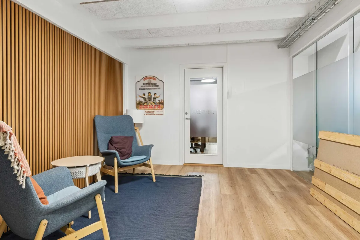 Funktionelt kontorlokal med to blå sæder og lyse trægulve. Plakat på væggen med en filmtitel. Glasdør og lyse loft. Høj kvalitet og moderne design.
