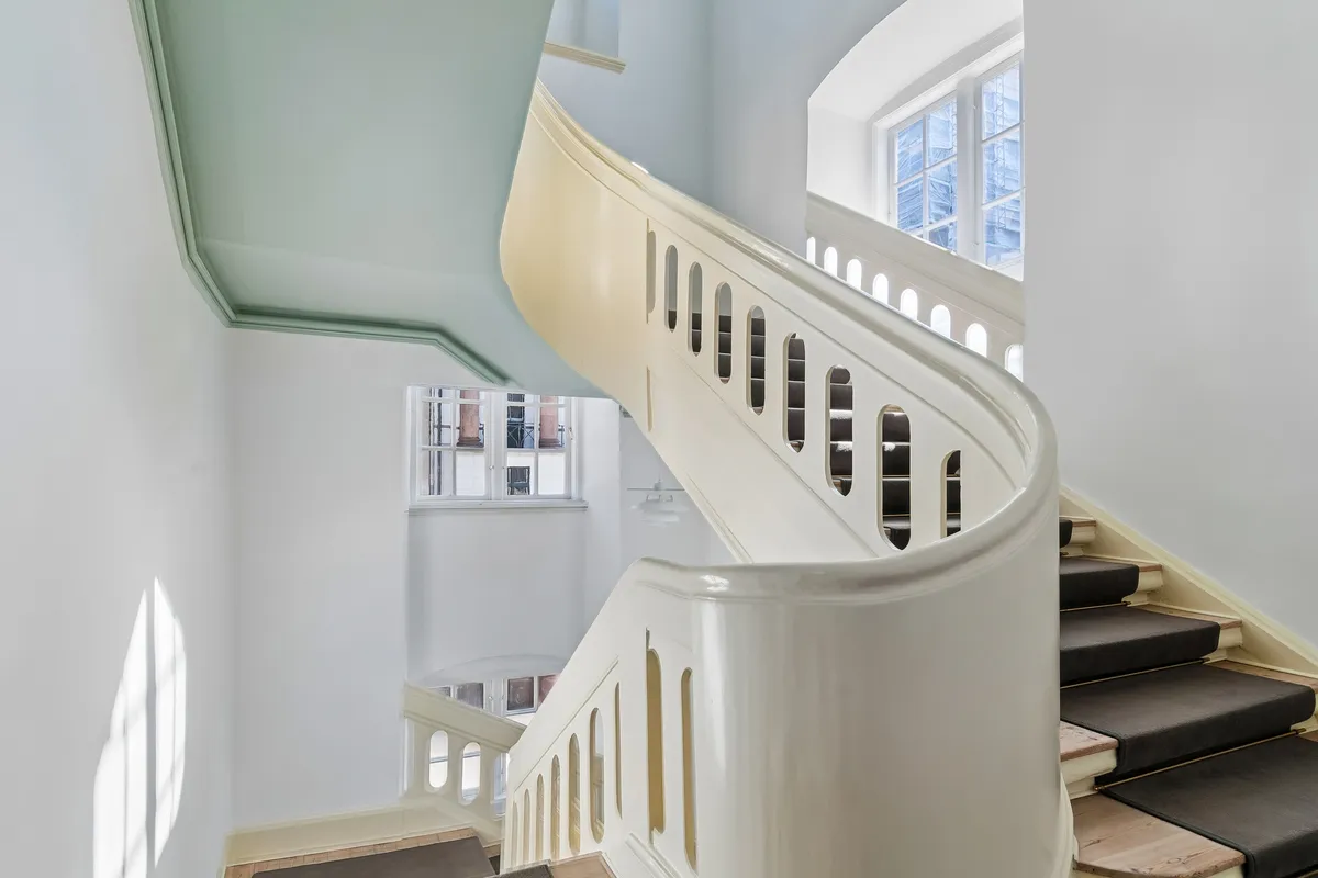 Elegant, hvid marmor-trappe med lysgrå loft og hvid forside. To vinduer i loftet, hvor man ser ud til gaden.