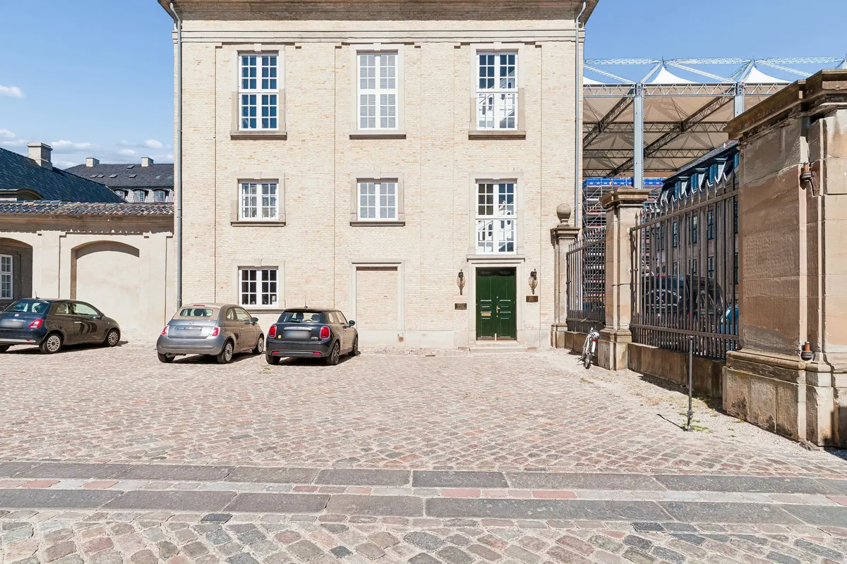 Tre biler parkeret foran en bygning med røde mursten og grønne døre i et fredeligt område i København