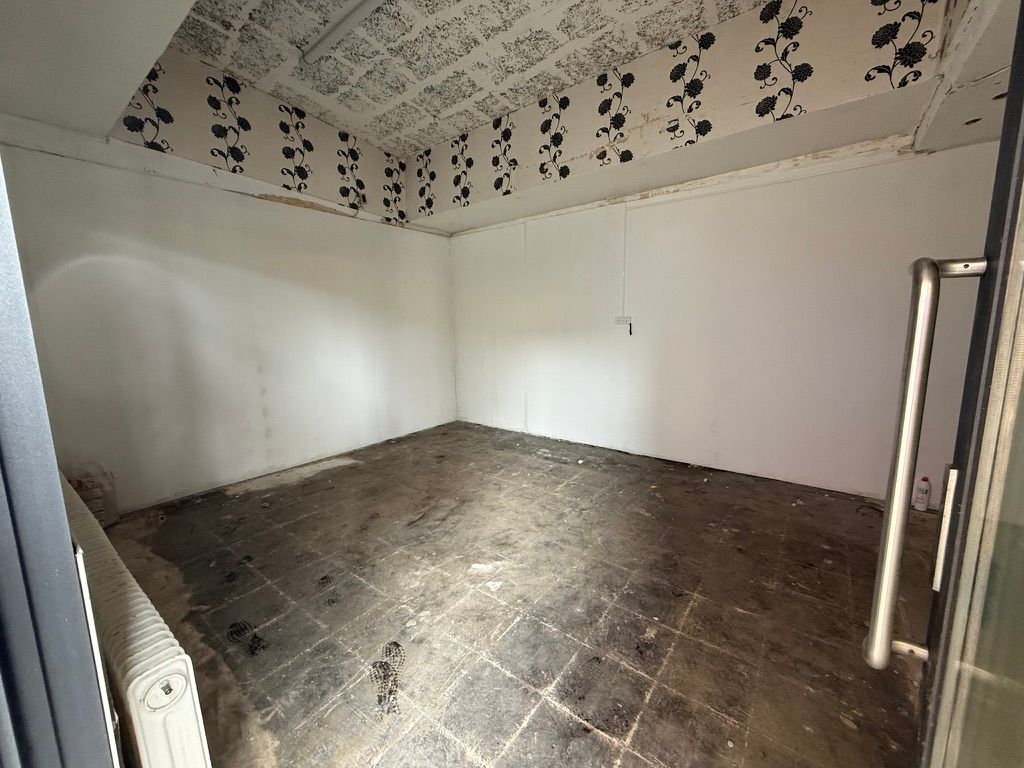 Et tomt rum med glat gulv, hvidt loft og vægge samt et enkelt radiator på en side og en dør til venstre