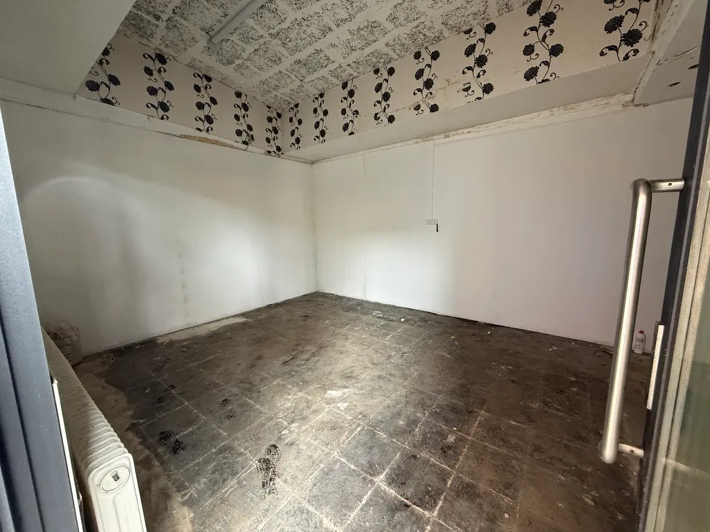 Et tomt rum med glat gulv, hvidt loft og vægge samt et enkelt radiator på en side og en dør til venstre
