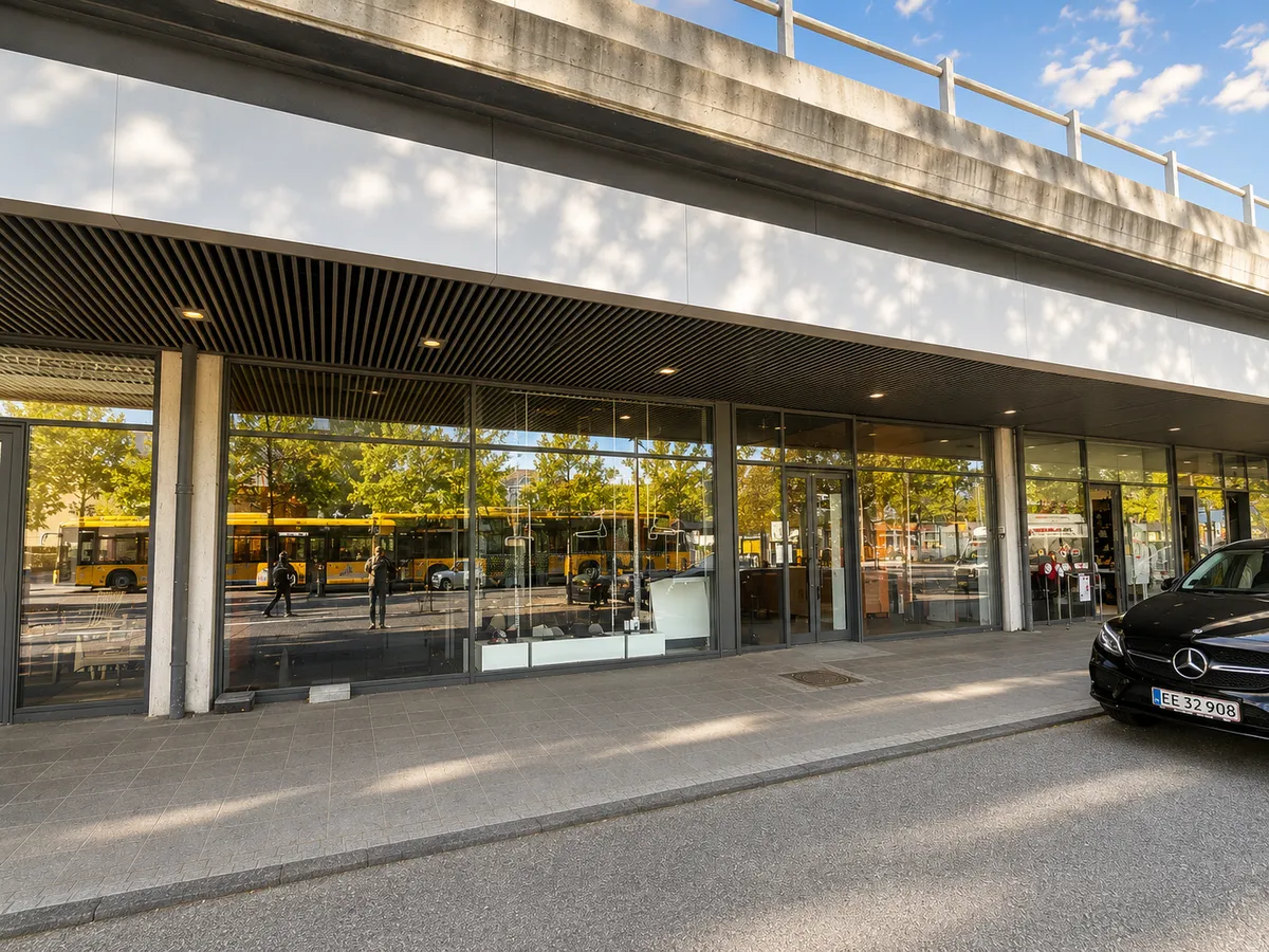 Mercedes bil parkeret foran bygning med store vinduer og overhængende bro med folk og busser i refleksion