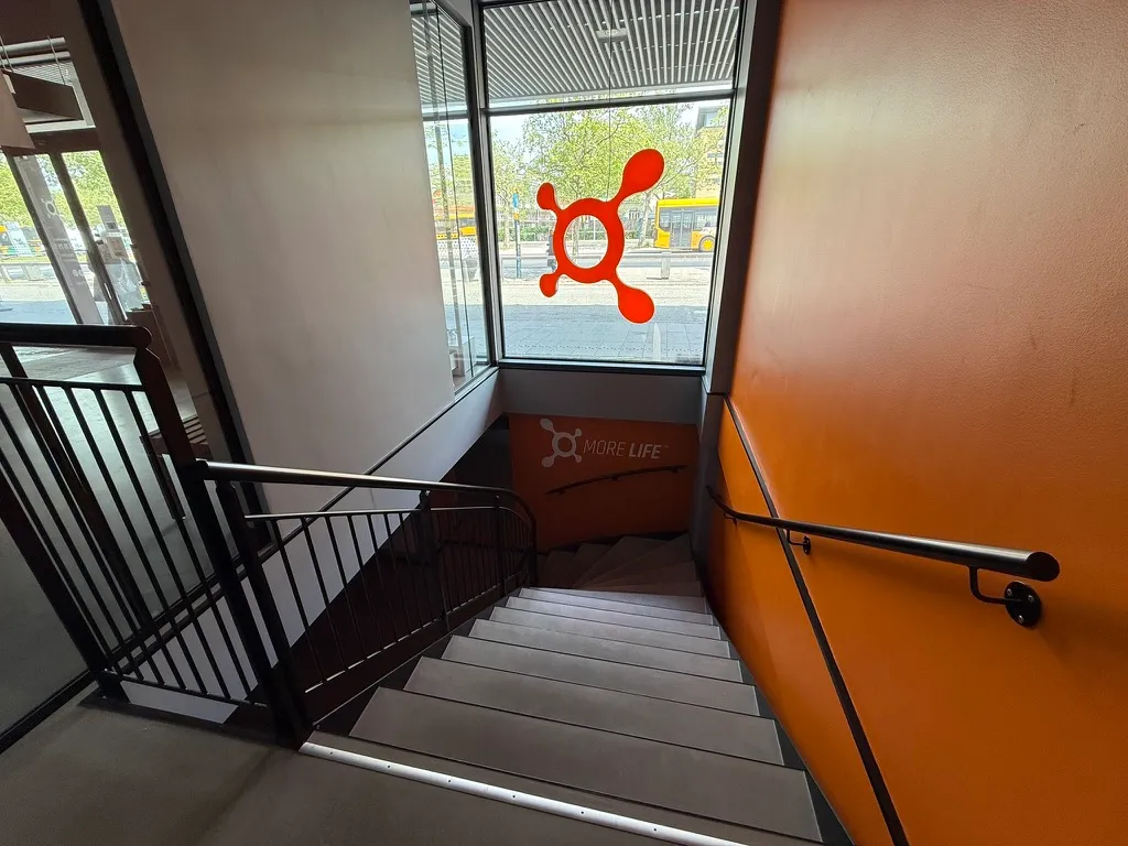 Trapper fører op til et fitnesslokale med en orange væg og en logo i vinduet, der viser teksten More Life. Stigerne har mørke håndtag