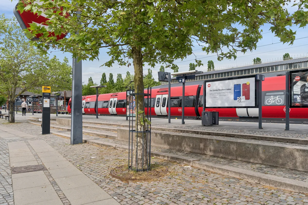 Lyst lejemål i nærheden af Klampenborg Station med smukke facader og grønne træer langs gaden og større reklameskilte