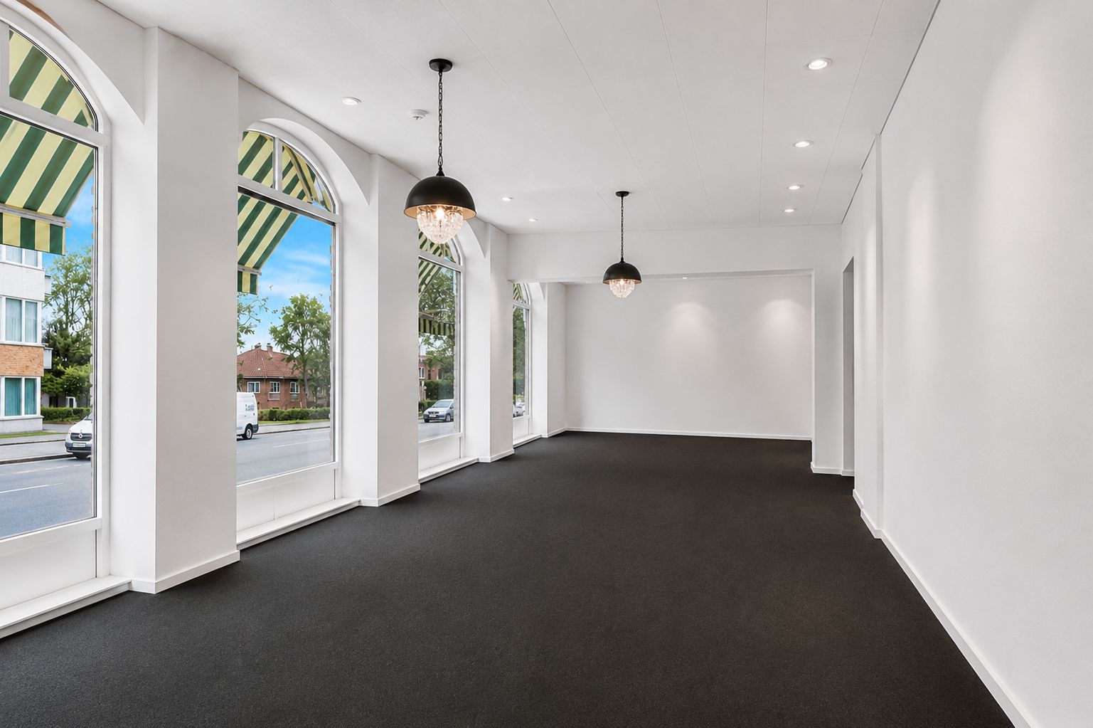 Lys stue med store vinduer og moderne lamper. Pæn gulvbelægning, hvidt loft og gulv og lysepunkter.
