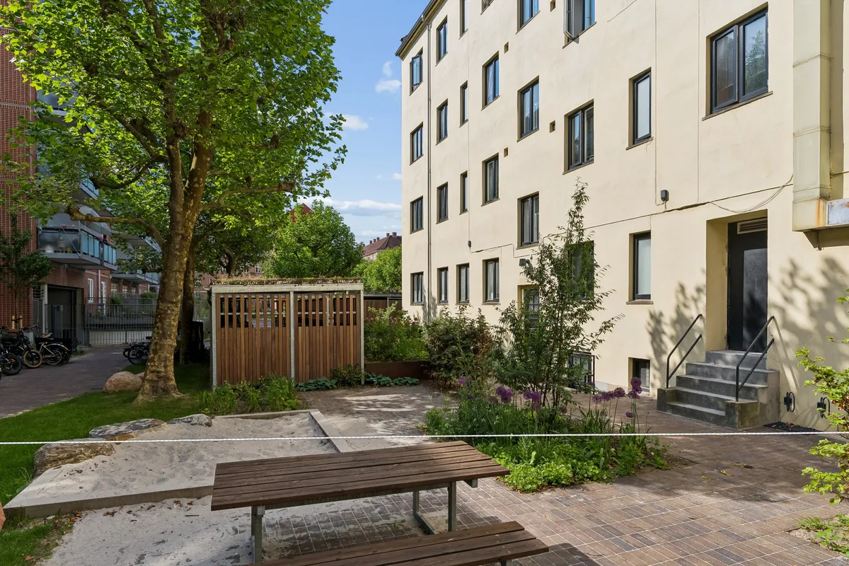Erhvervsandel til salg på Vennemindevej med terrasse, træbænke og grønne planter i baggrunden og et moderne bygning med mange vinduer