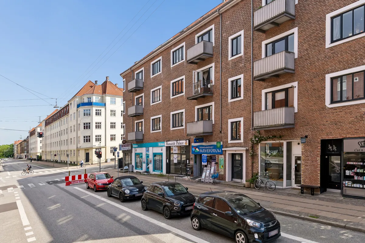 En bilparkeret gade med små biler og butikker og caféer på hjørnet. En cykelhvirvel, der fører til en trafikrygning med trafiklys og vejskilte