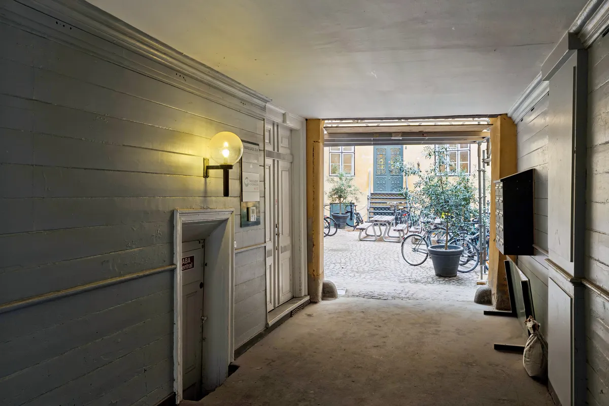 Lys pære på væg, åbne dør til gård, søjler, ruder og vinduer, blomster, skovl og skovlende søjle, træbord og stol, cykler, postkasse og postkasse og postkasse