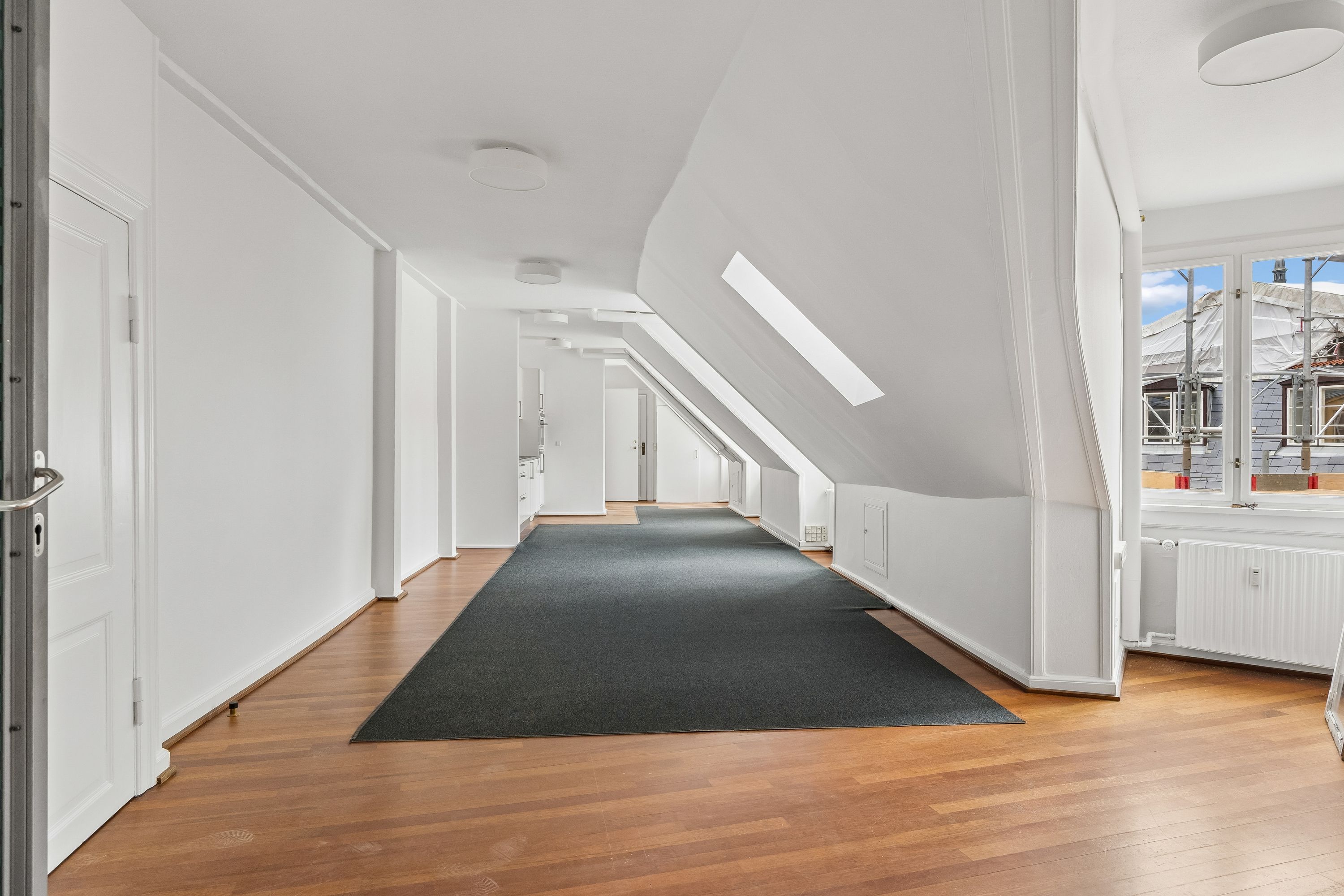 Lyst kontor med hvide vægge og lyse lofter med lysekroner og lyskabler. Parketgulve og luksuriøs gulvbelægning i stuen. Køkken med hvide vægge og radiatorer.