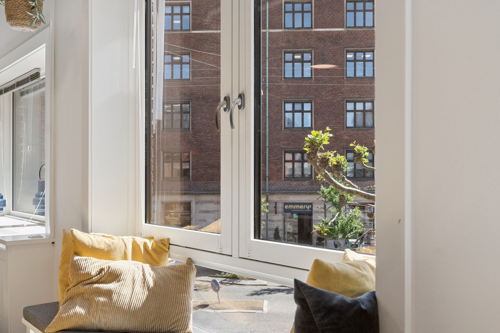 Lys kontorlejlighed med lysegult sæde, smukke vinduer og udsigt til bygning med Emmerys skrift. Lys refleksion på glas.