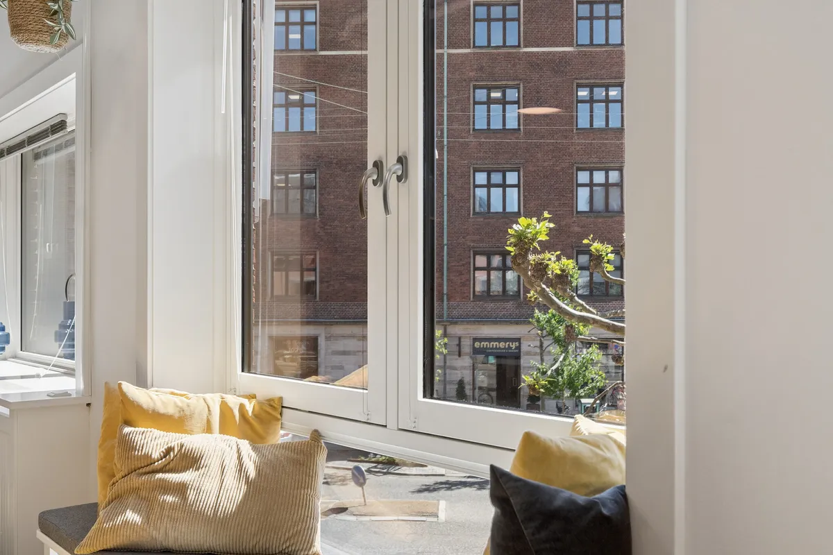 Lys kontorlejlighed med lysegult sæde, smukke vinduer og udsigt til bygning med Emmerys skrift. Lys refleksion på glas.