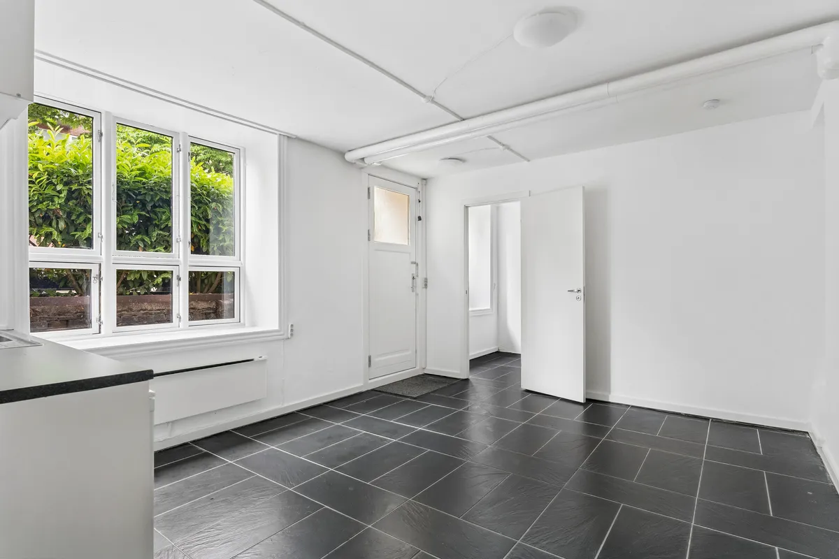 Lej kontorlejlighed på Harsdorffsvej 7, Frederiksberg. 35 m² med hvidt interiør og smukke sort gulv. Vindue med udsigt til buske og sten. Hvidt køkken og moderne design.