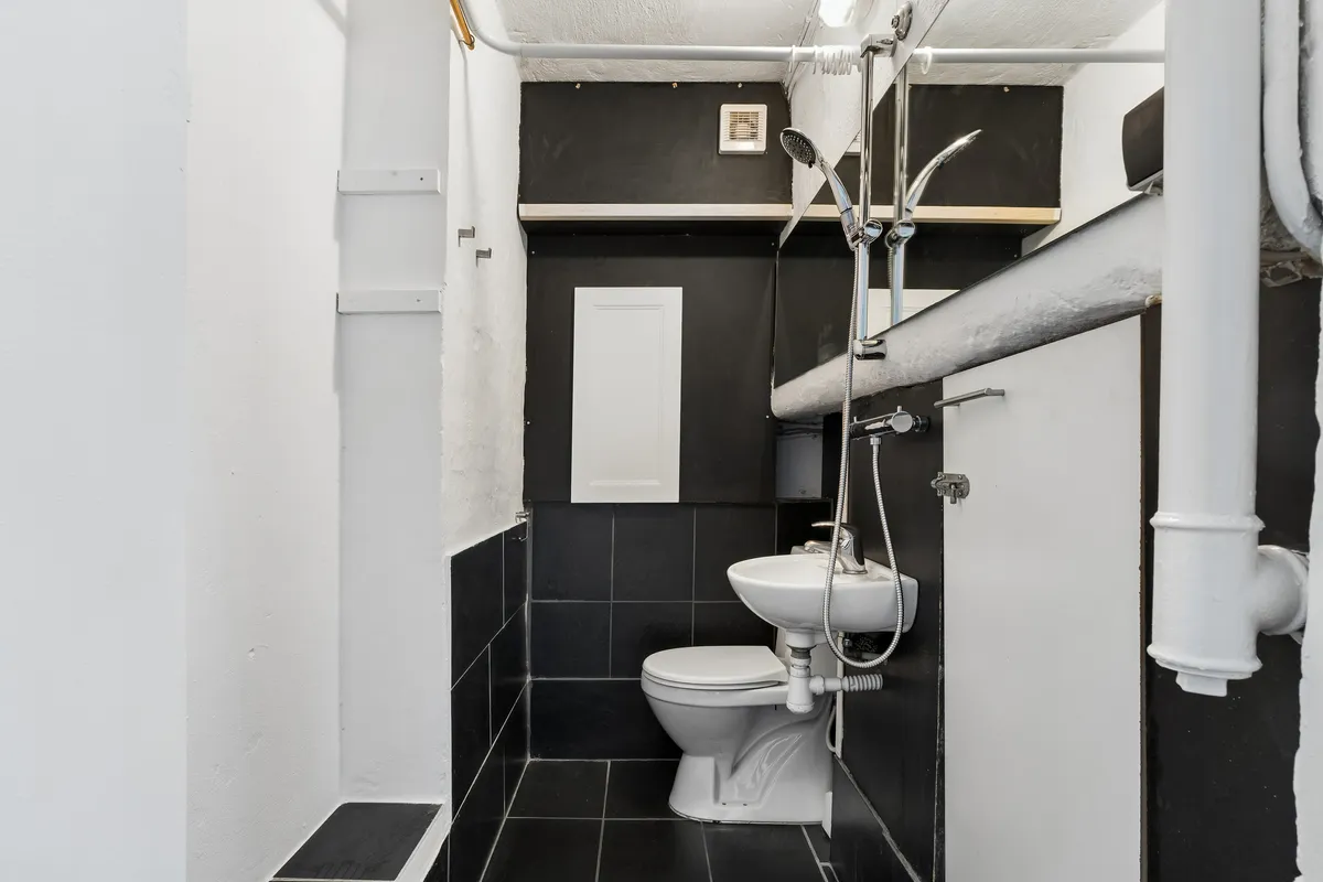 Værelse med hvidt toilet, sort beklædning og hvidt badekar. Håndklædetørrer og hvidt badekar i toilettet. Væggen er hvid og sort, og der er to hængehylder.