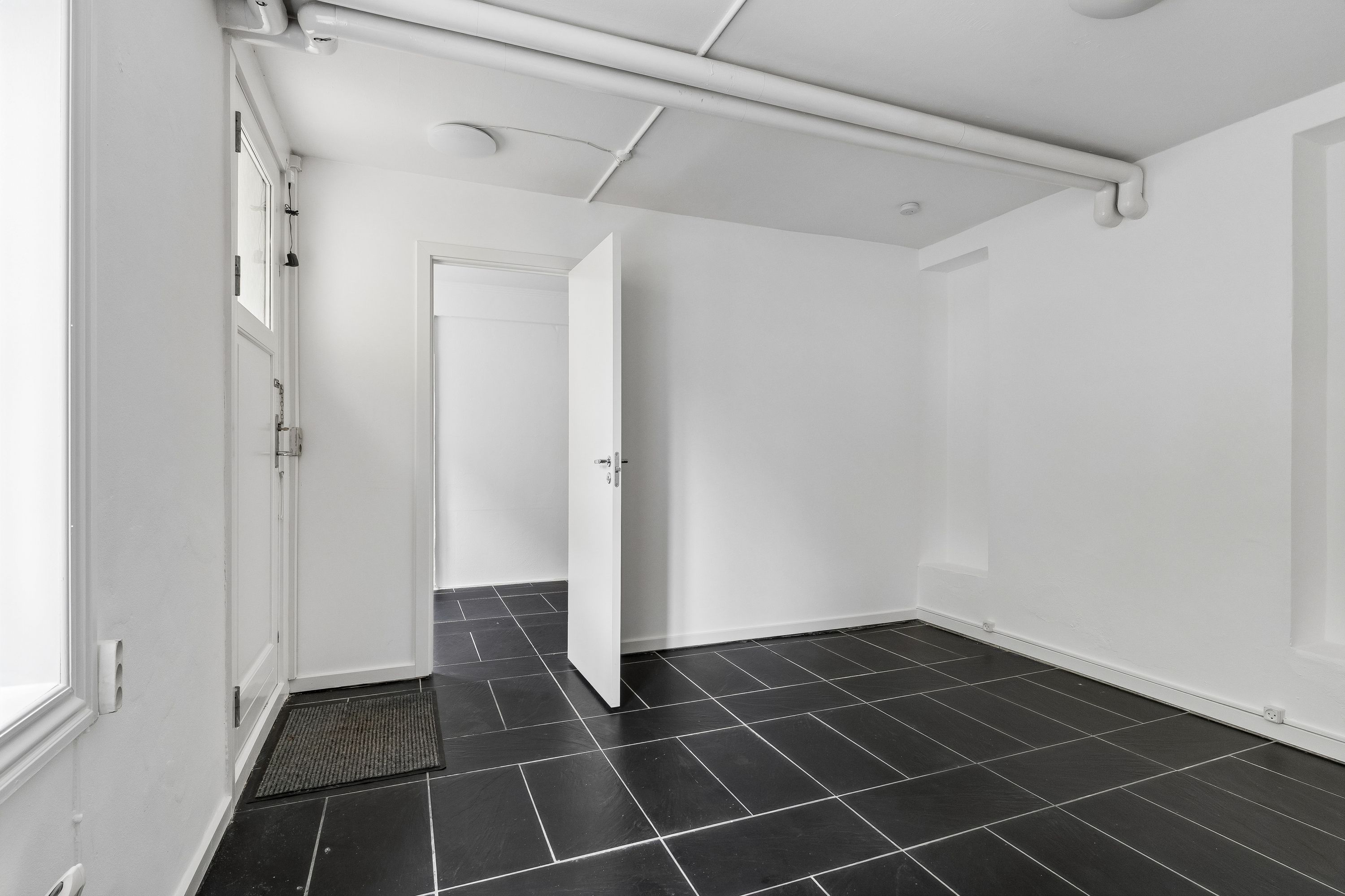 Rent og minimalistisk kontorlokal i lejemål på 35 m² med lyse vægge og sort gulv samt åbne døre og en lysafkapping på loftet