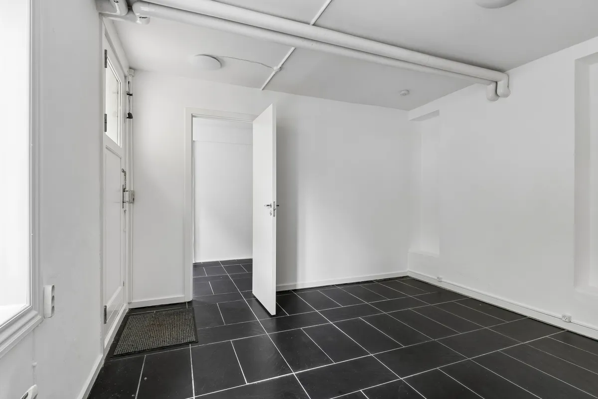Rent og minimalistisk kontorlokal i lejemål på 35 m² med lyse vægge og sort gulv samt åbne døre og en lysafkapping på loftet